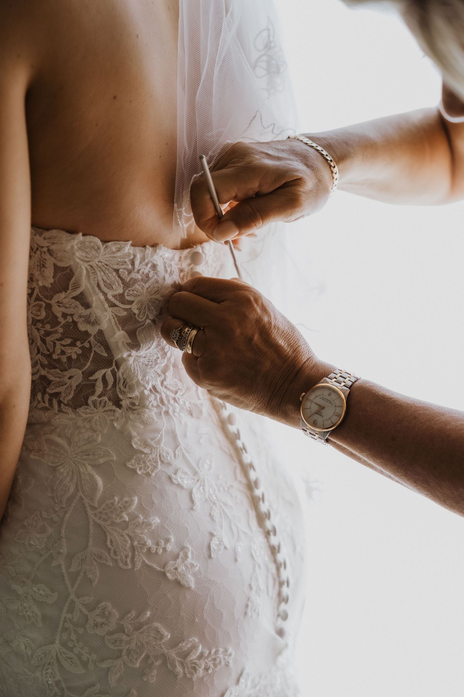Close-up of hands buttoning intricate lace details on wedding dress.