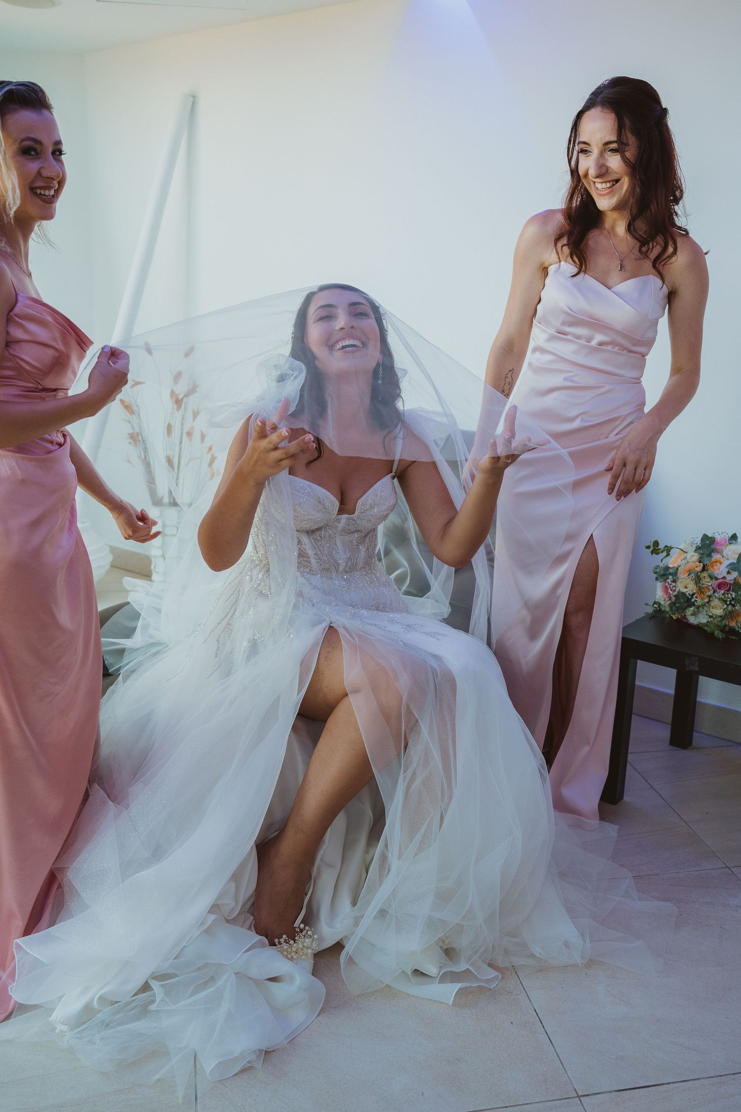 Candid moment of bride and bridesmaids laughing together during wedding preparations.