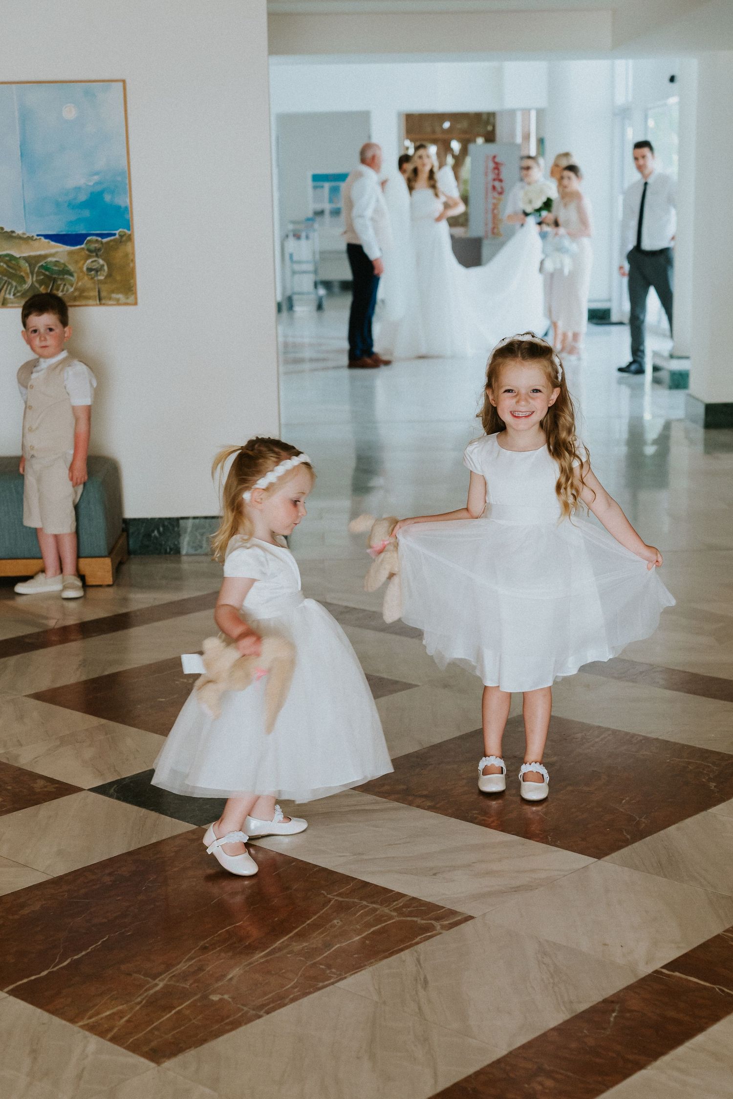 Young attendants in white dresses twirling on a checkered ballroom floor during a wedding celebration.