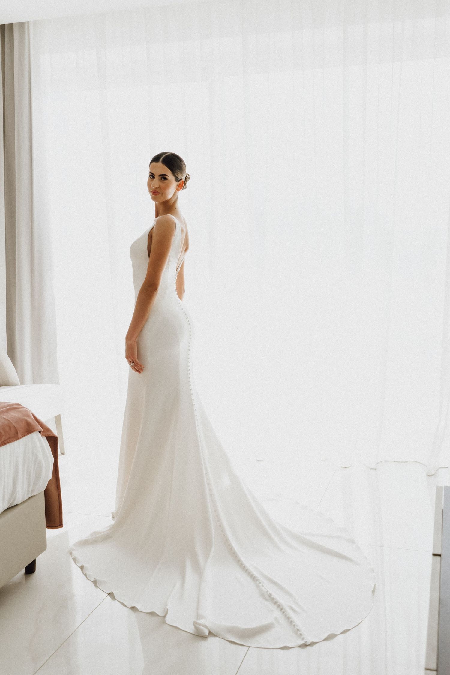 Elegant white wedding dress with a dramatic train photographed against a bright interior setting.