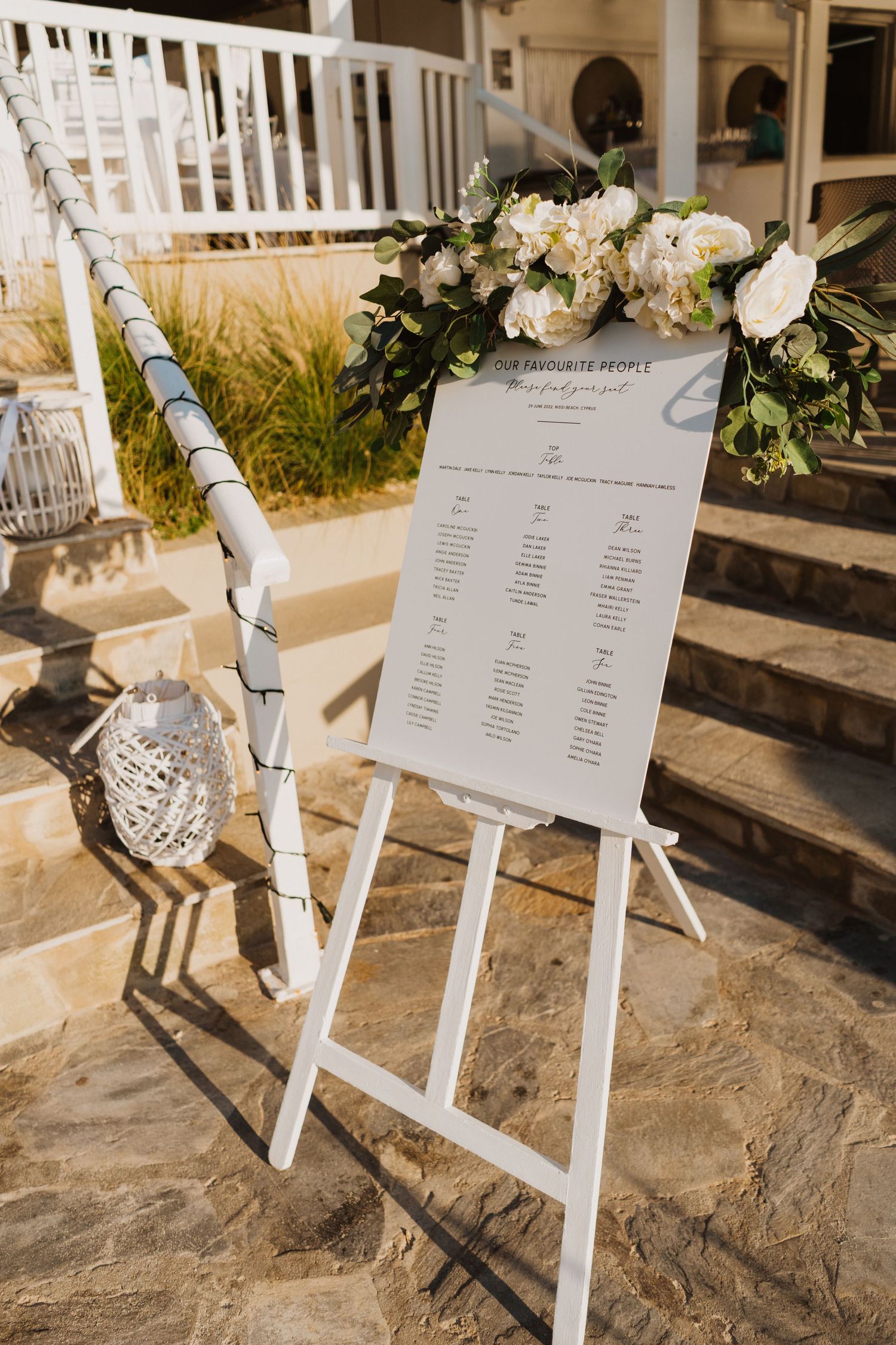 Wedding seating chart displays mounted on white easels against a stone backdrop with decorative floral accents.