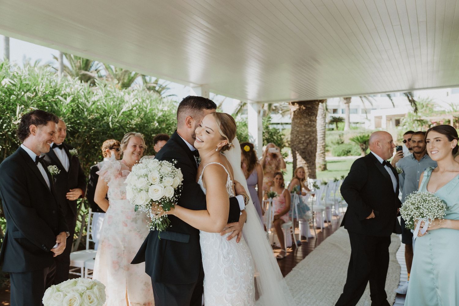 Wedding party celebrates during a joyful ceremony under a covered outdoor venue.