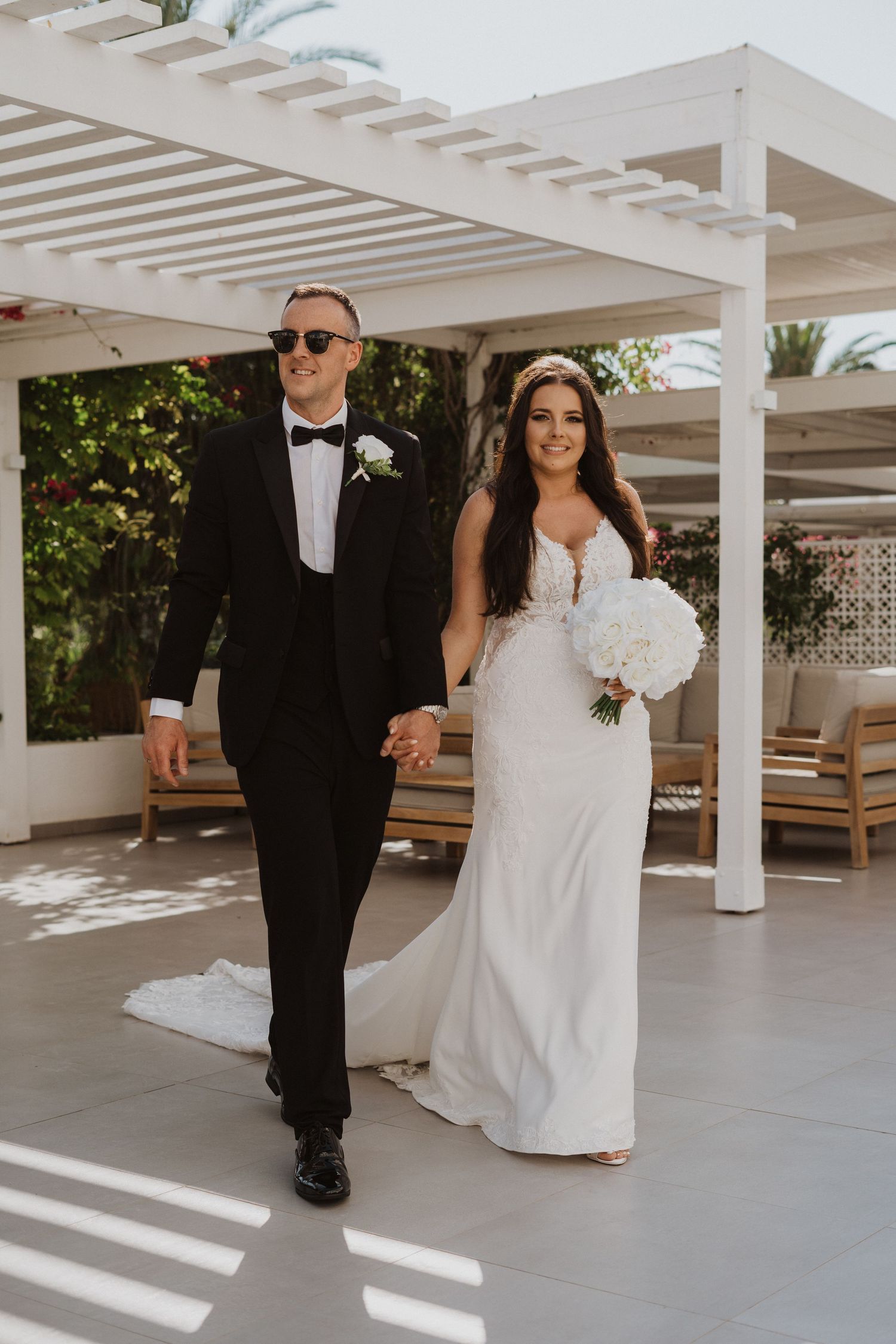 A couple shares a joyful moment under a white pergola during their beach wedding.
