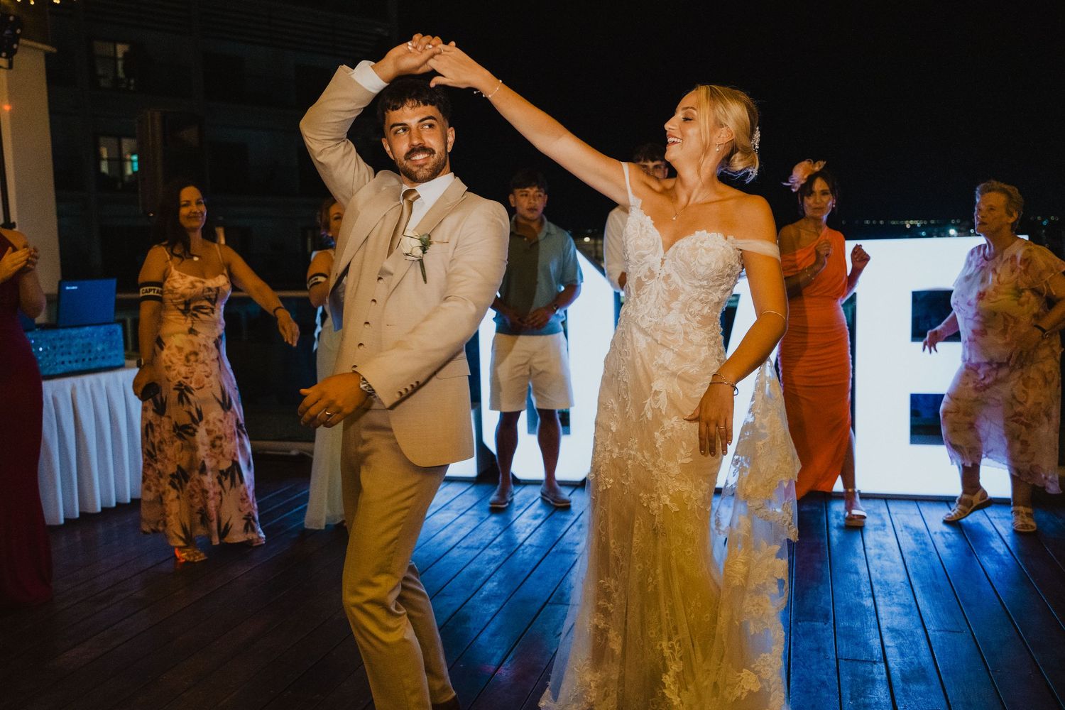 Couple performing upbeat dance moves at reception with LOVE sign in background.