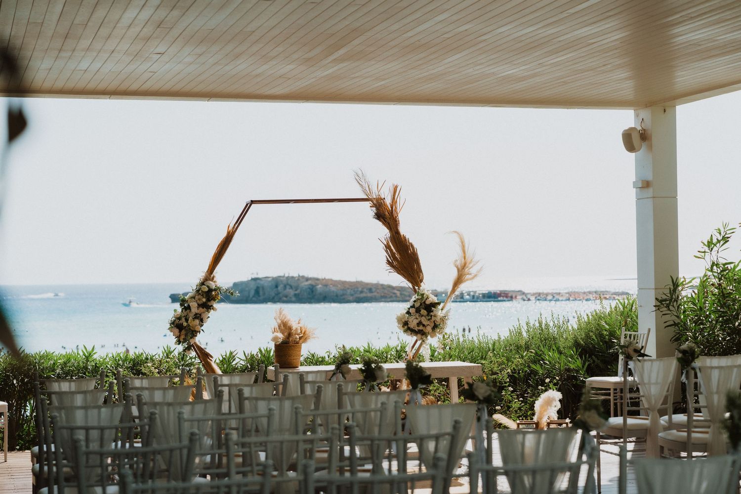 Wedding ceremony setup with wooden arch and white chairs overlooking the ocean.