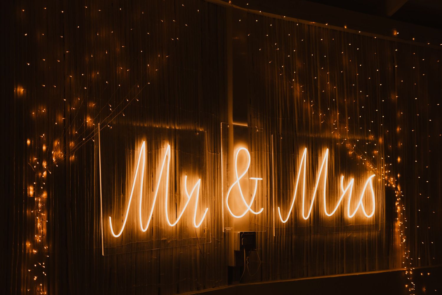 Illuminated 'Mr & Mrs' neon sign against fairy lights creating a romantic wedding backdrop.
