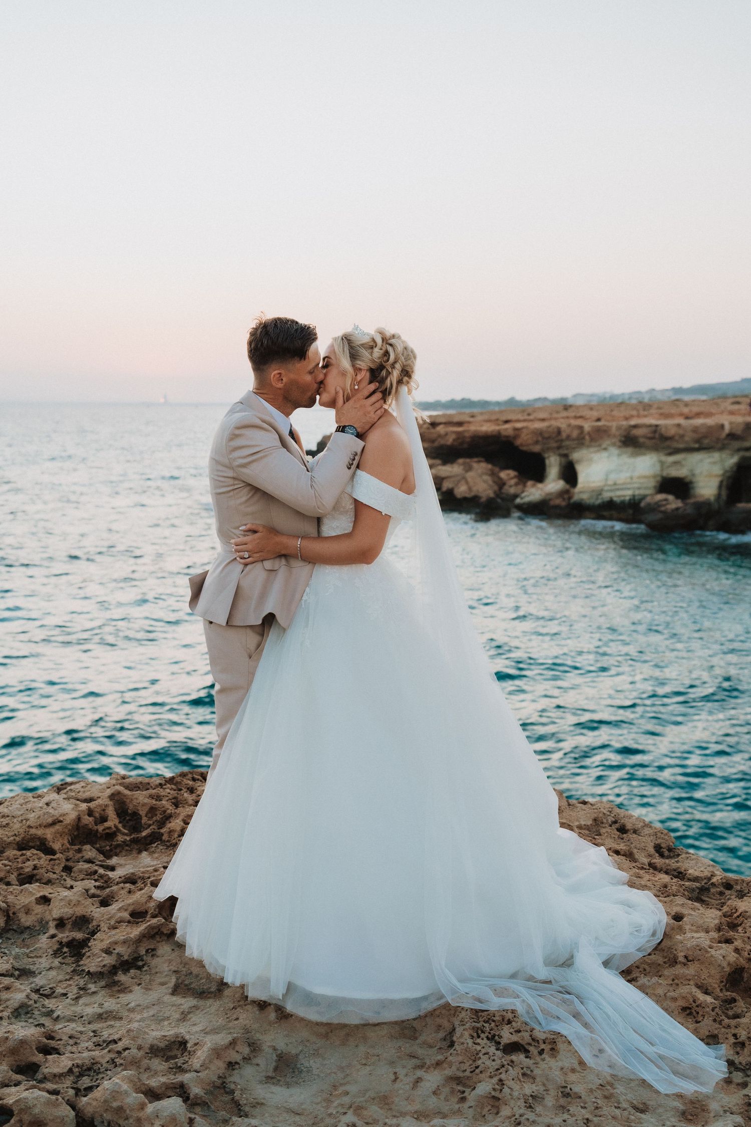 Romantic coastal wedding photo with dramatic cliff backdrop during golden hour.
