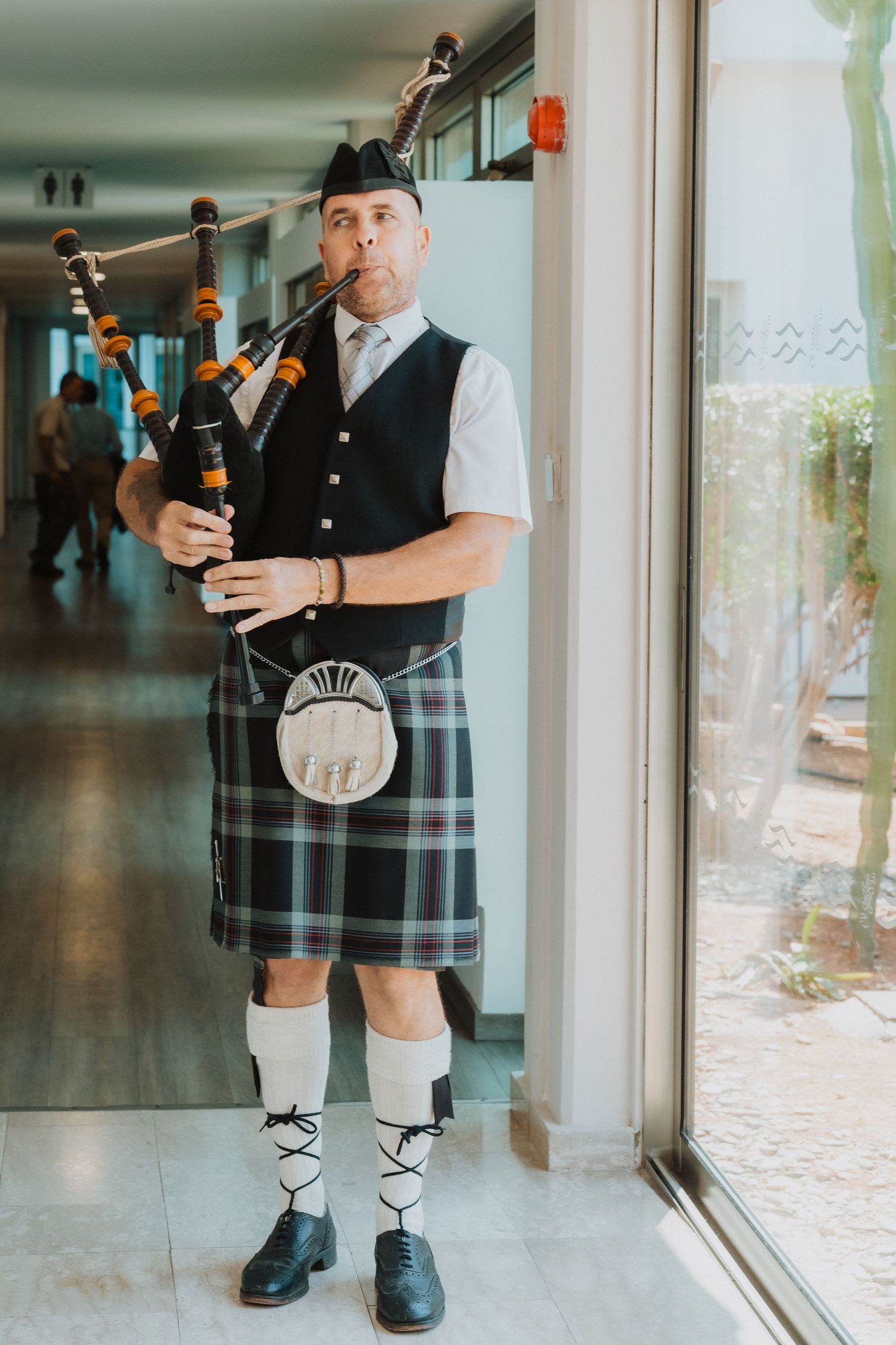 Bagpiper in traditional Scottish attire plays in a hallway.