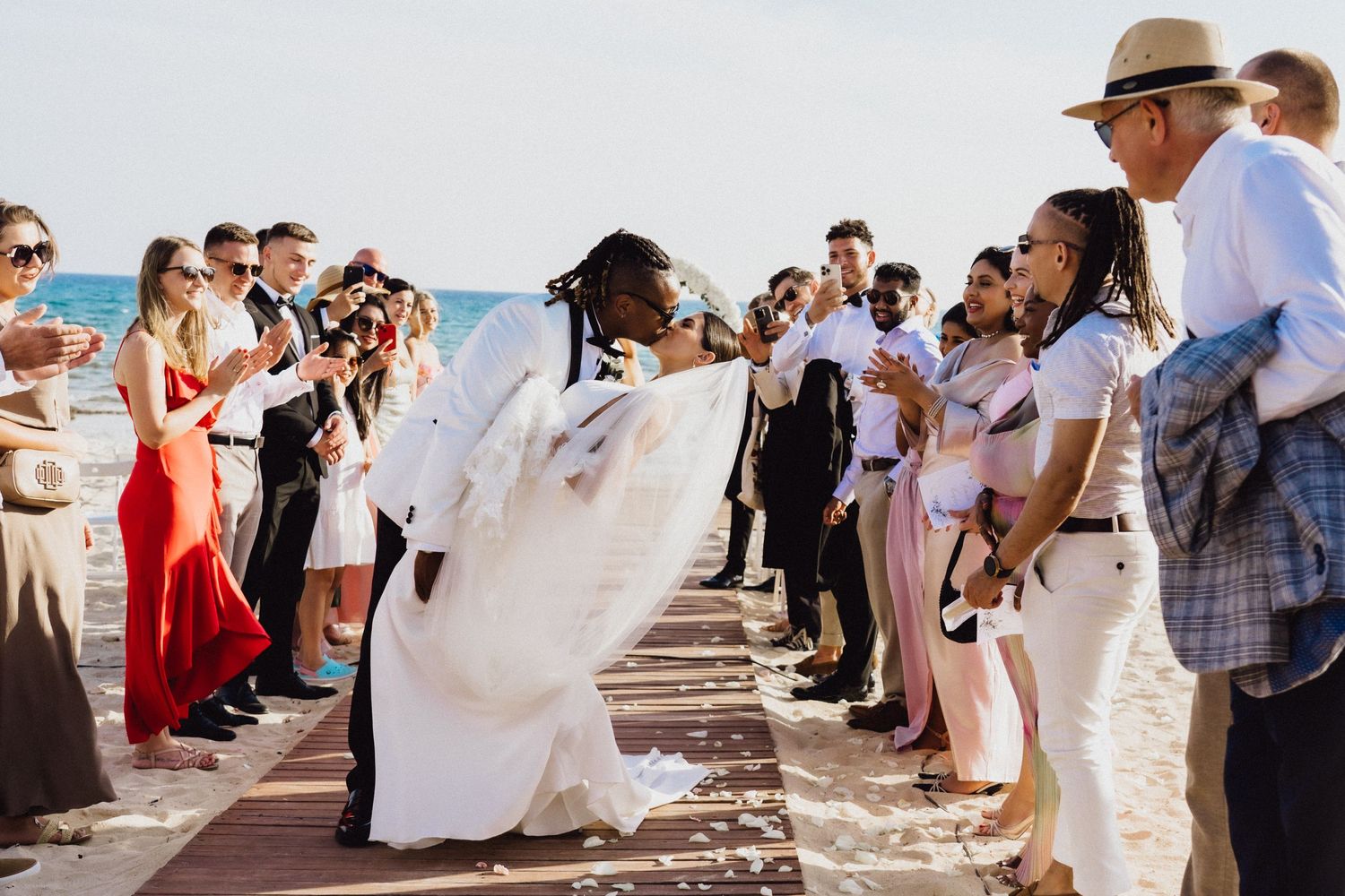 Wedding celebration dance on beachfront boardwalk with guests cheering.