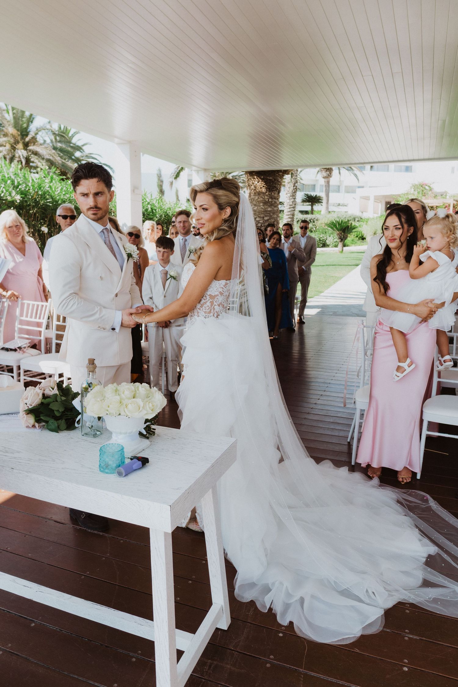 A wedding couple dances together on a covered porch during their first dance while guests watch from the sides.