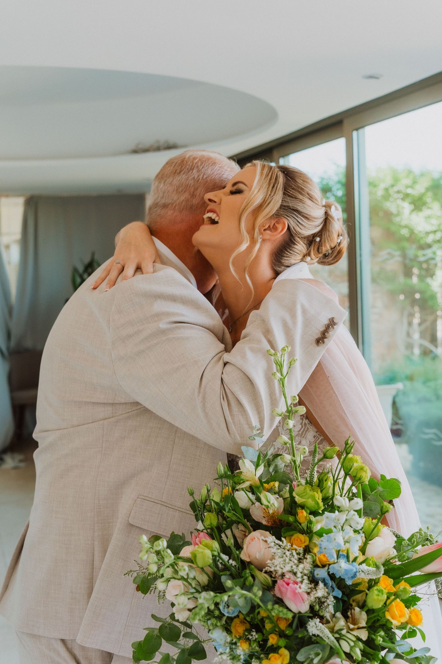 A tender embrace at a wedding with a beautiful colorful spring bouquet featuring pink, yellow and white flowers.