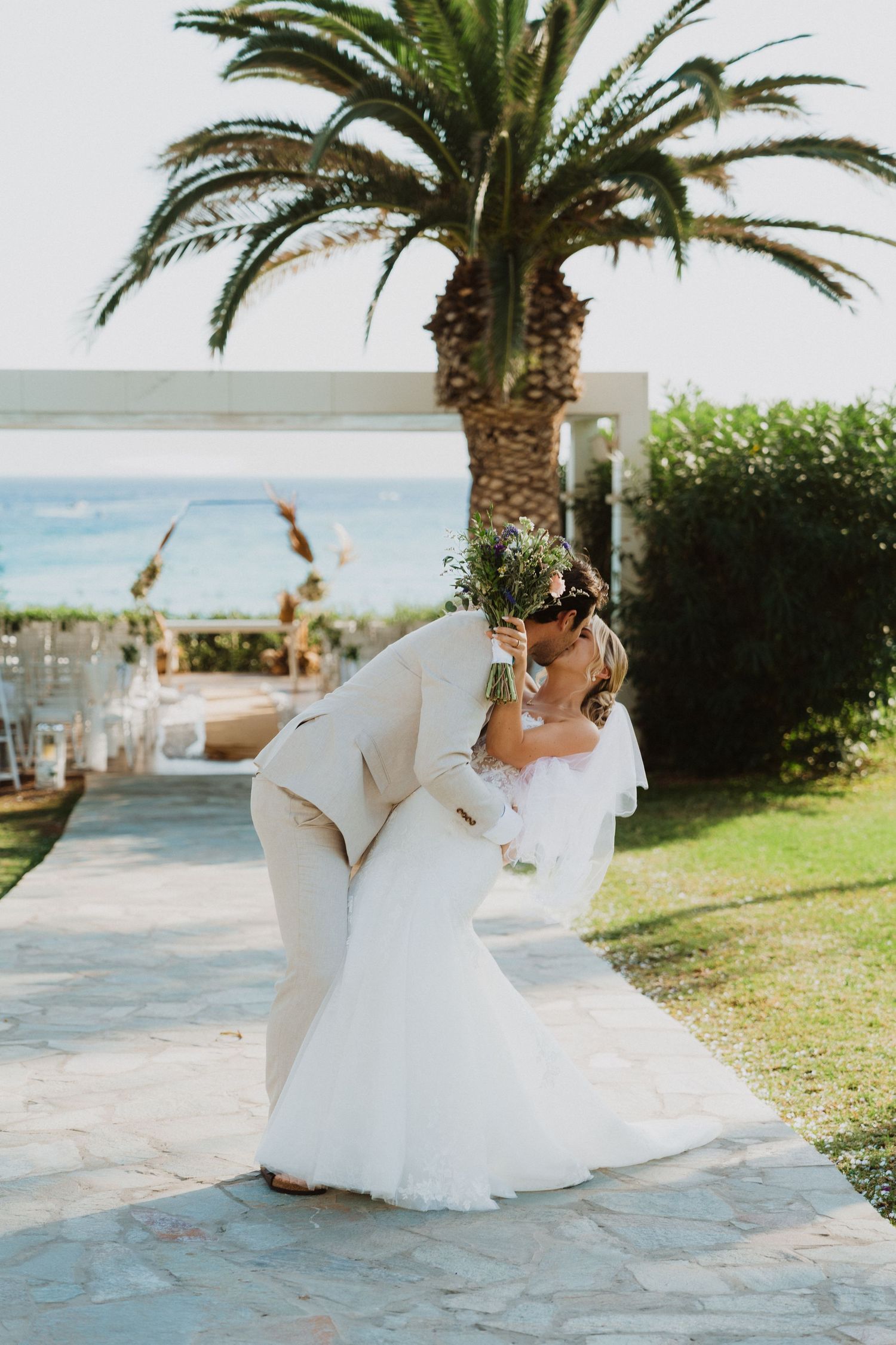 A romantic dip pose under a palm tree at an oceanfront wedding venue.