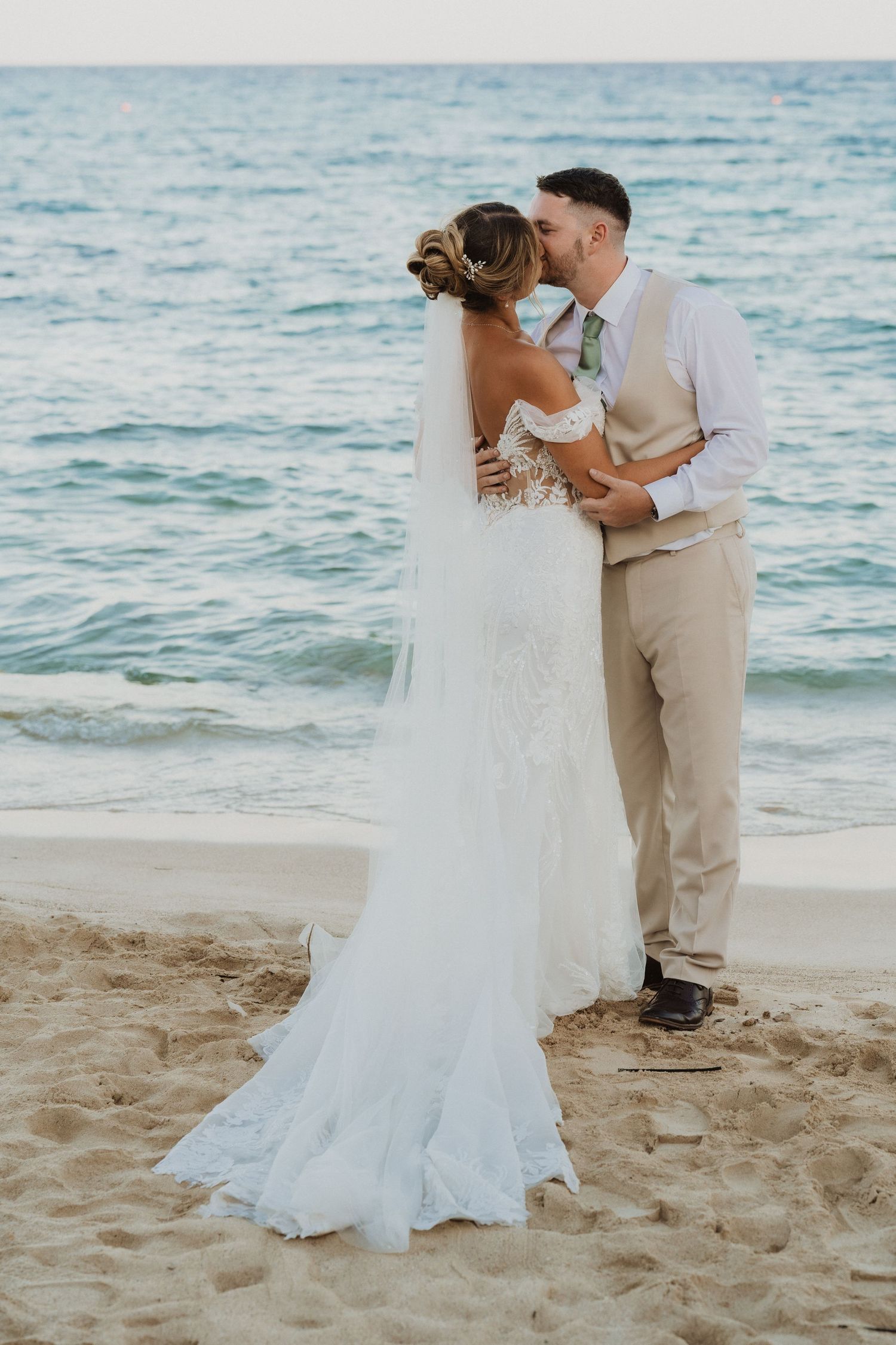 A romantic beach wedding scene with a couple dancing on sandy shores by turquoise waters at sunset.