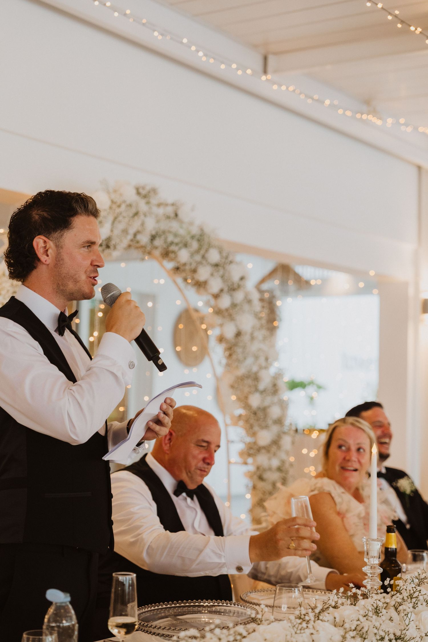 Wedding party members giving speeches at an elegantly decorated reception table.