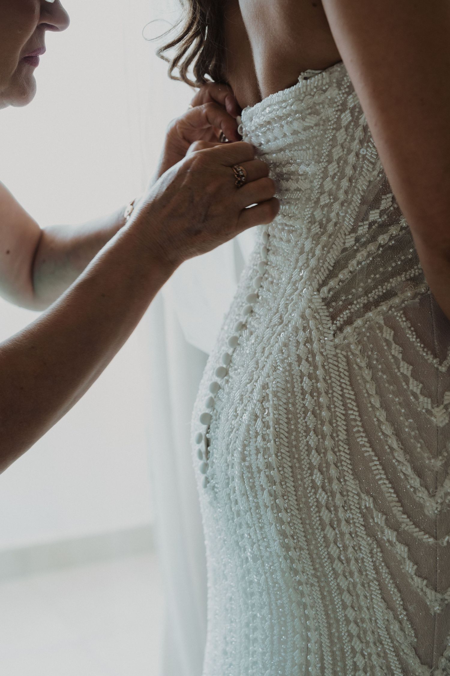 Mother helping bride button up her intricate lace wedding dress before the ceremony.