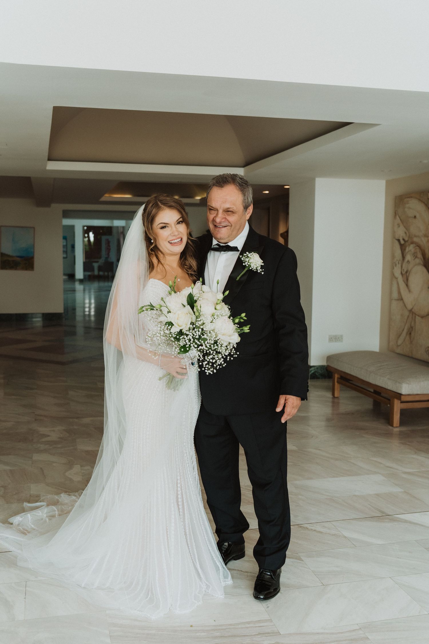 Father of the bride proudly walking daughter in elegant white wedding gown with long veil.