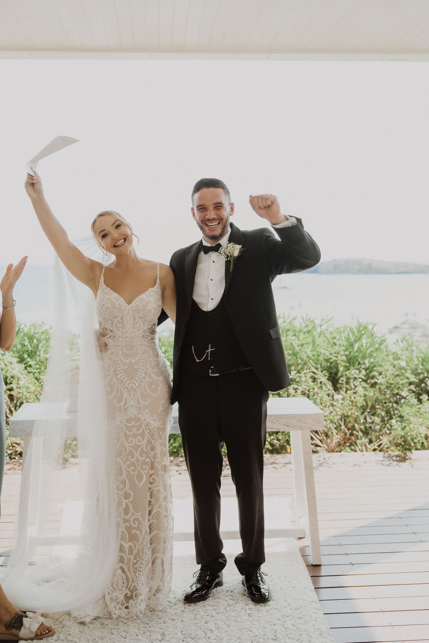 Joyful wedding celebration on a bright outdoor terrace with palm trees in the background.