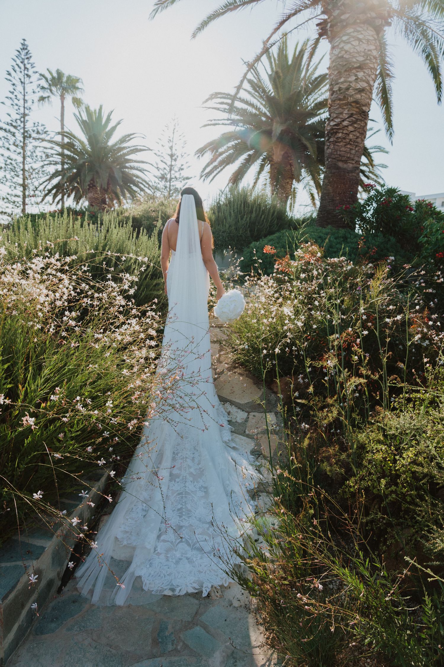 A flowing white wedding dress photographed among tropical flowers and palm trees.