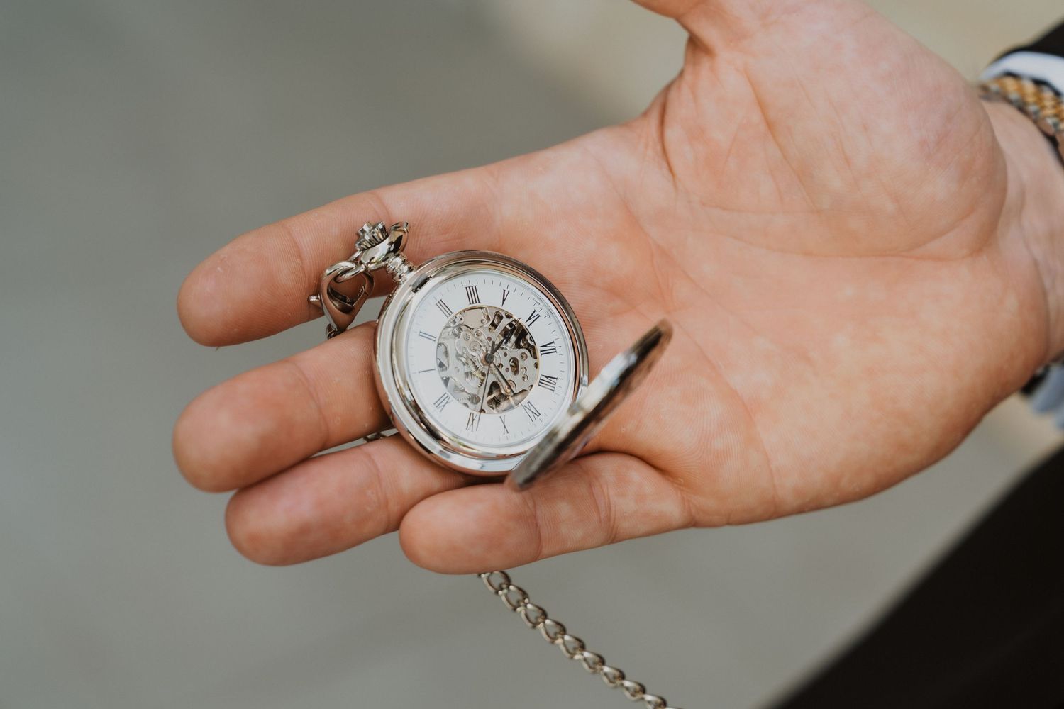 A silver pocket watch with exposed mechanical gears rests in an open palm.