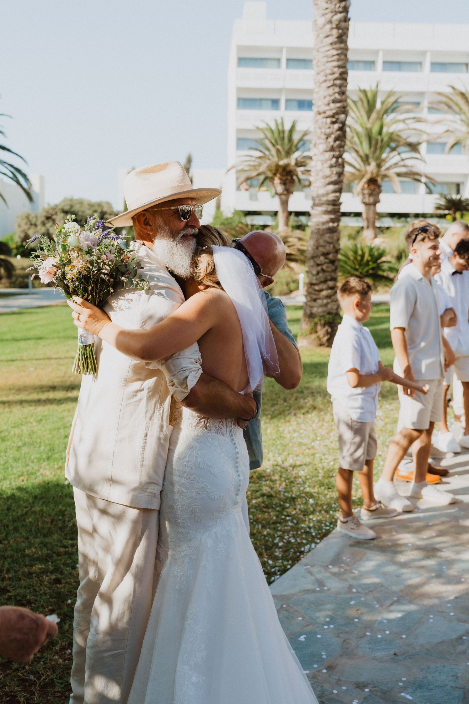 Wedding celebration with guests and wedding party on a sunny day with palm trees in the background.