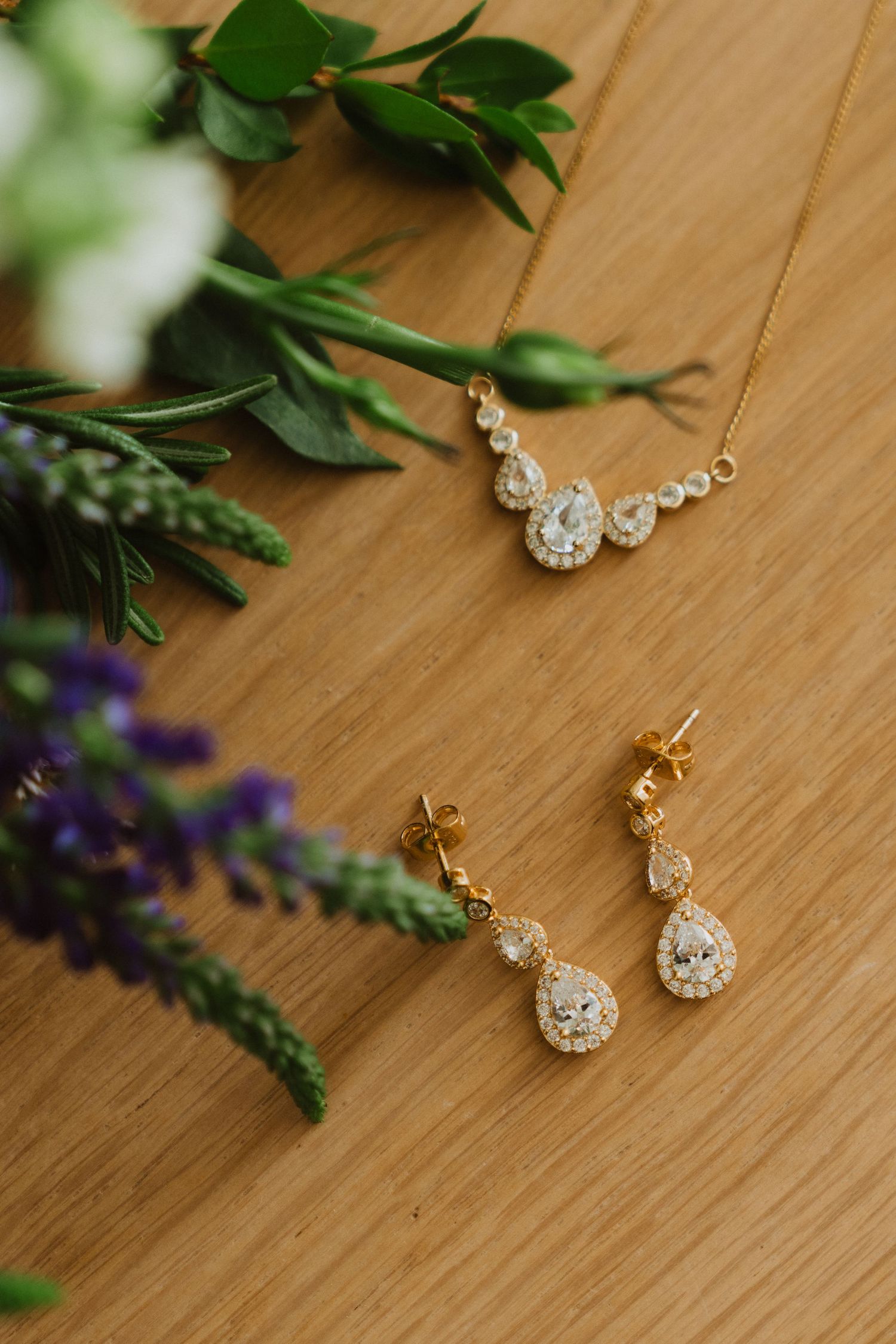 Crystal teardrop necklace and matching earrings set against greenery and purple flowers.