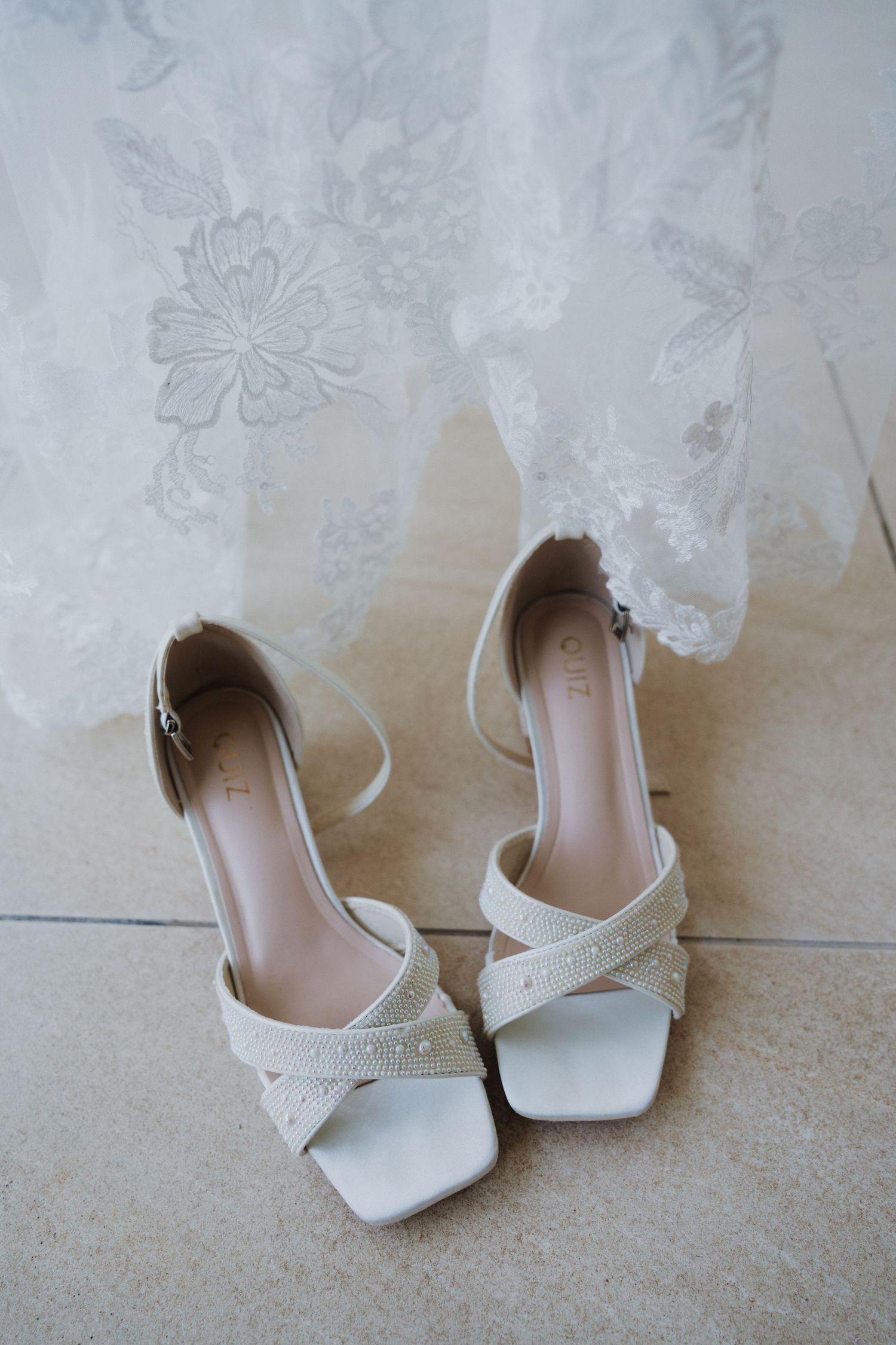 Elegant white bridal shoes with delicate lace detailing against wedding dress fabric.
