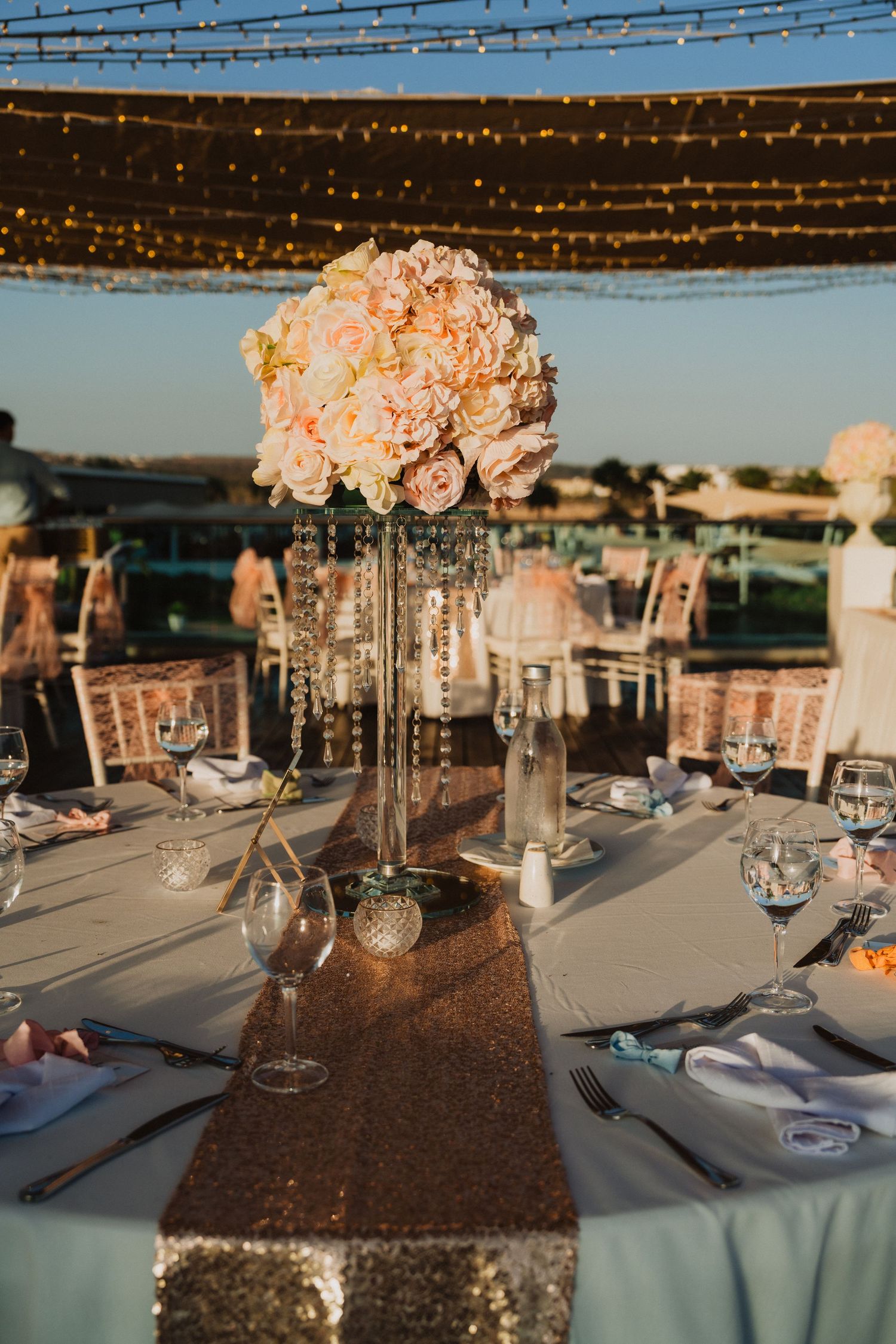 Wedding reception tables decorated with crystal centerpieces and string lights overhead.
