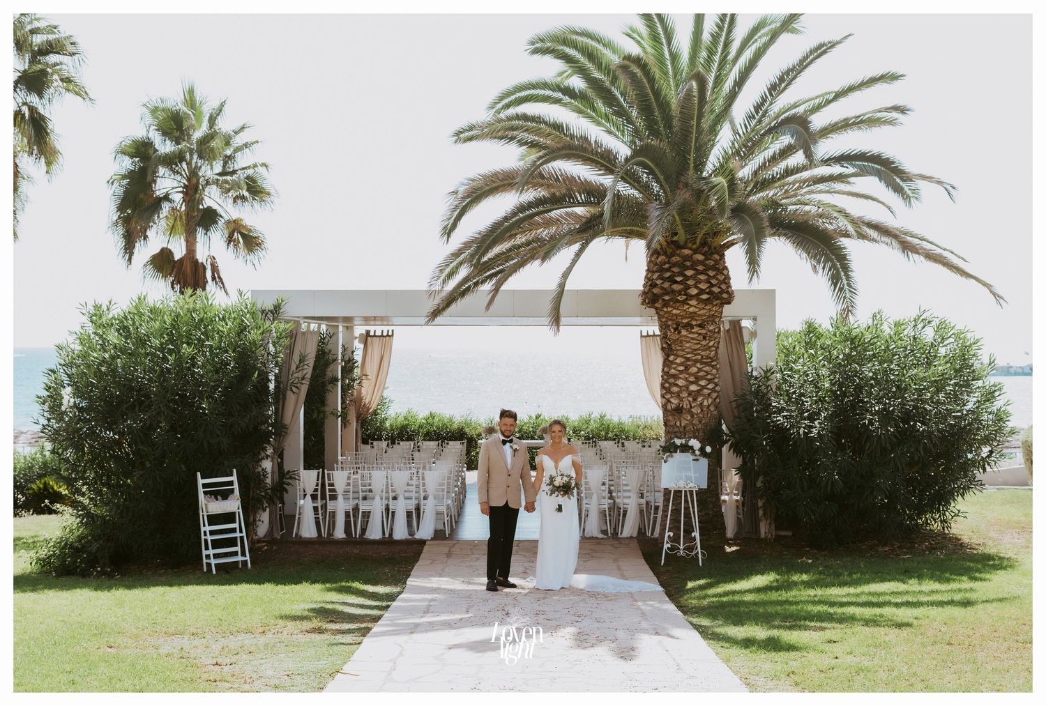Wide shot of a wedding ceremony setup with white chairs and palm trees framing an outdoor venue.