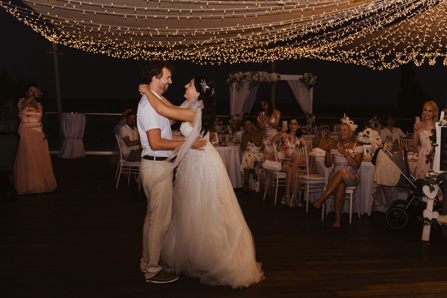 A romantic wedding dance moment captured under string lights at an outdoor reception.