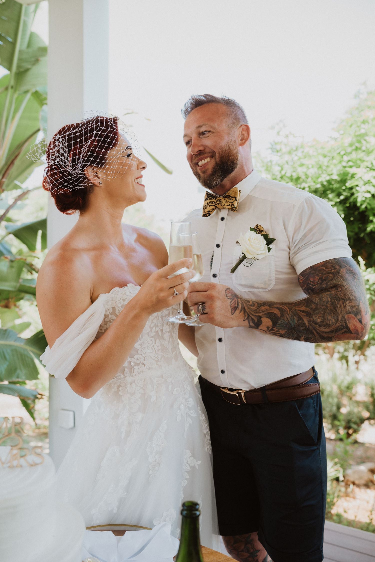 Couple in wedding attire toasting with champagne glasses outdoors.