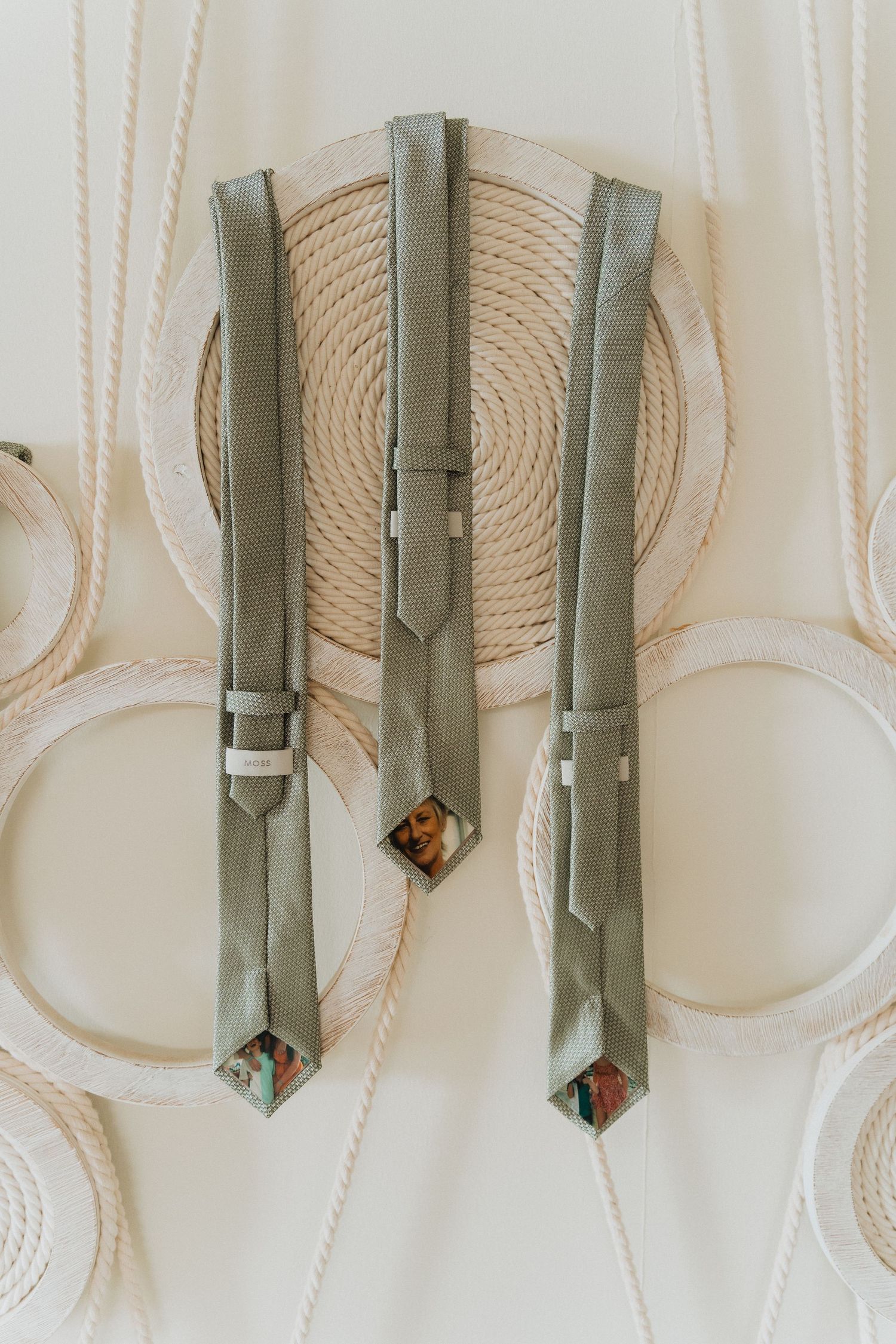 Three sage green men's suspenders arranged on a cream textured surface with decorative accents.