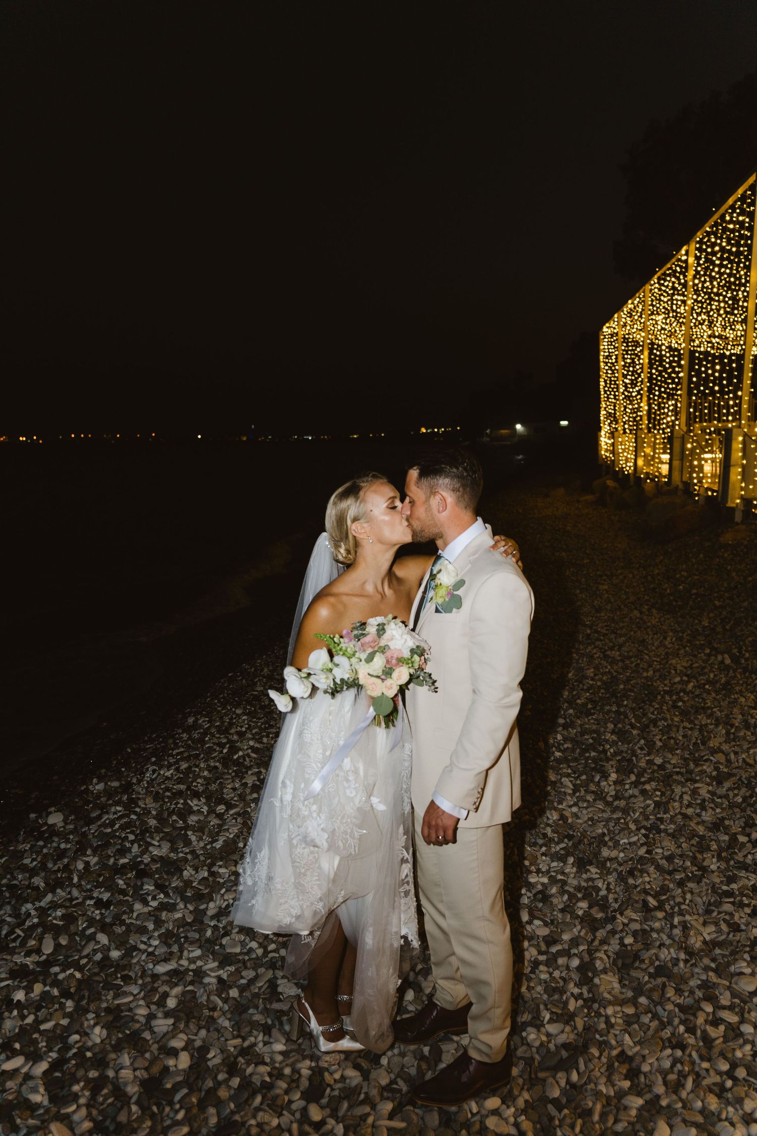 Intimate wedding moment captured against illuminated backdrop on beach at night.