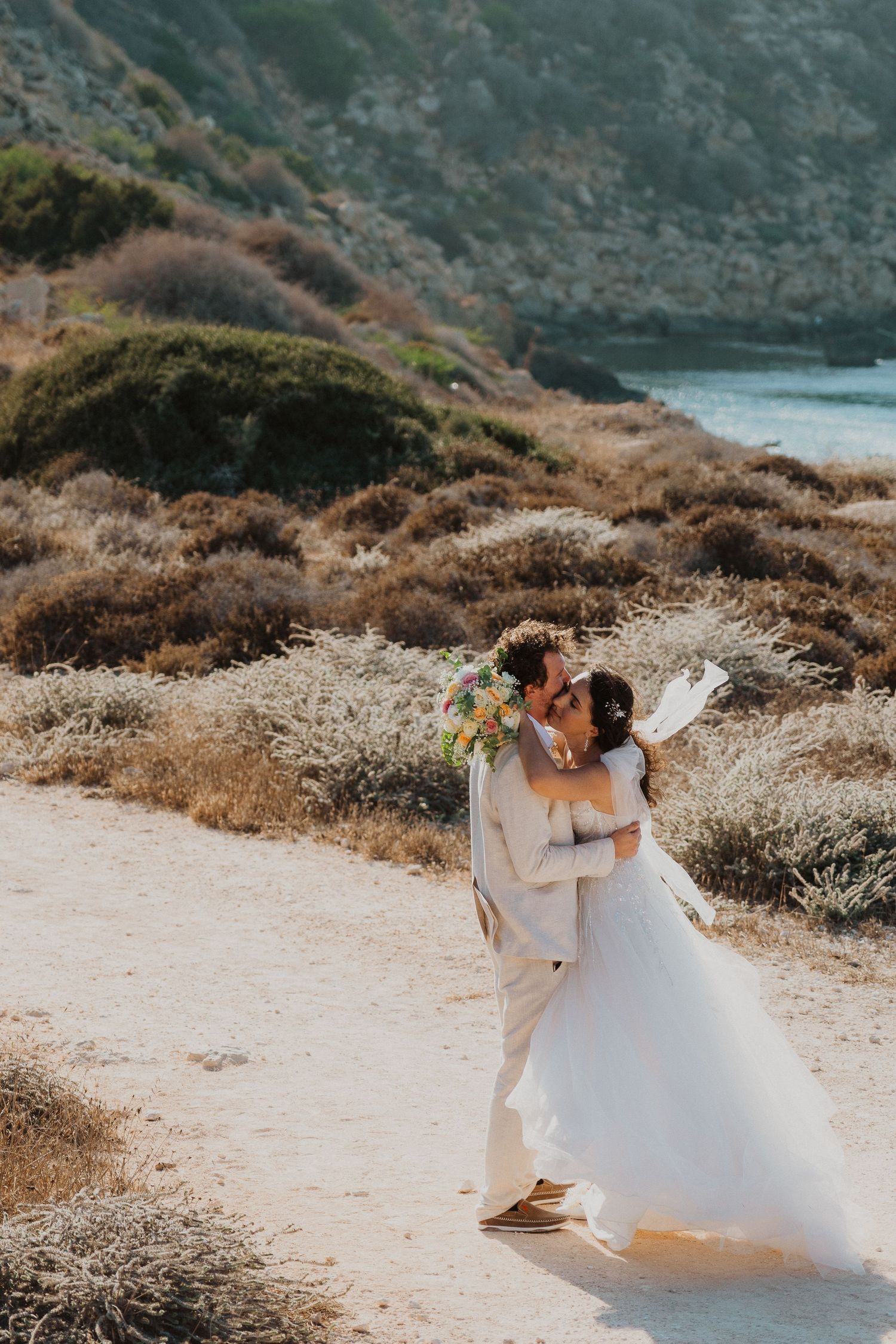 A couple shares a romantic moment on a coastal trail overlooking the ocean on their wedding day.