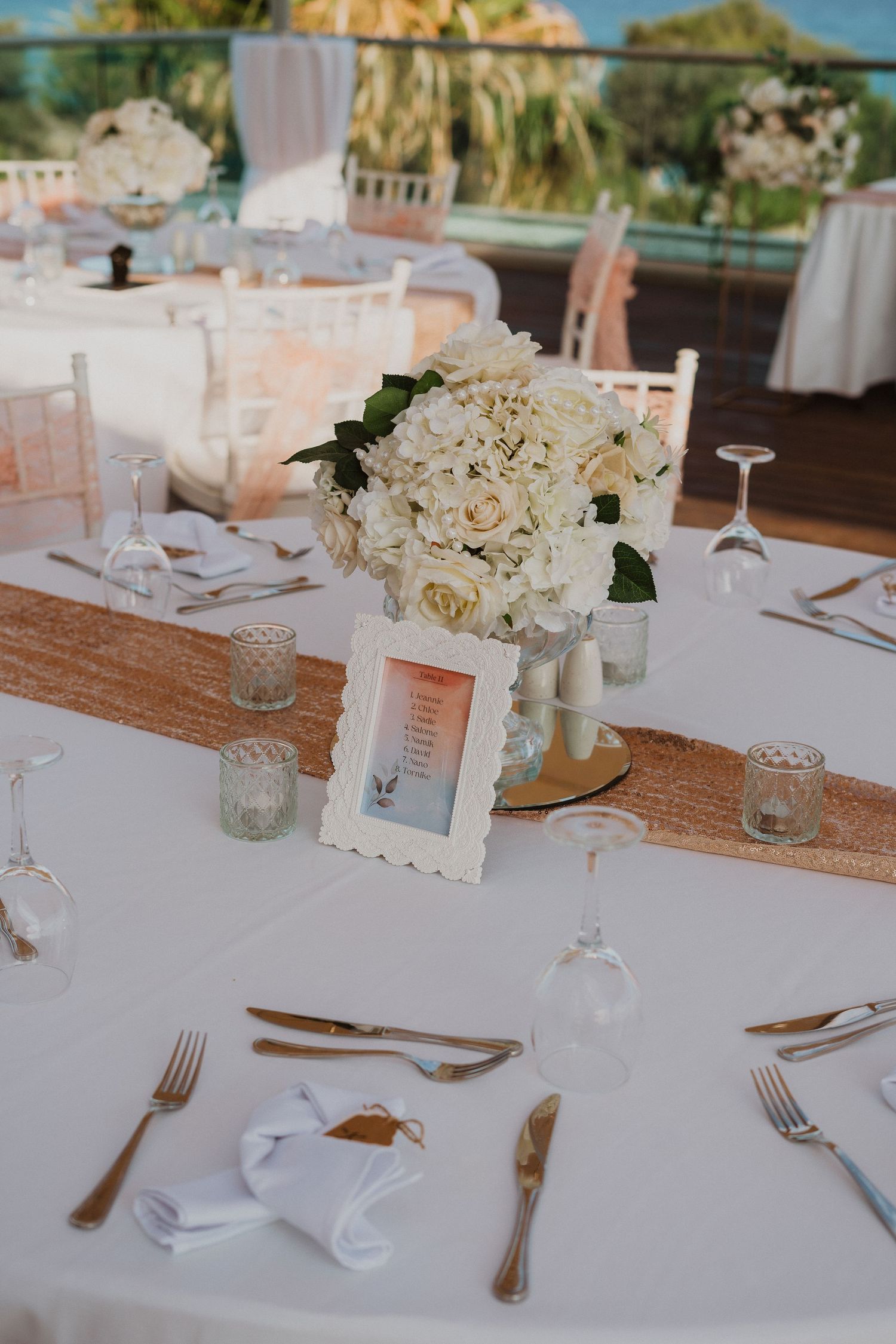 Elegant wedding table setting with white hydrangea centerpiece, burlap runner and crystal glassware at outdoor venue.