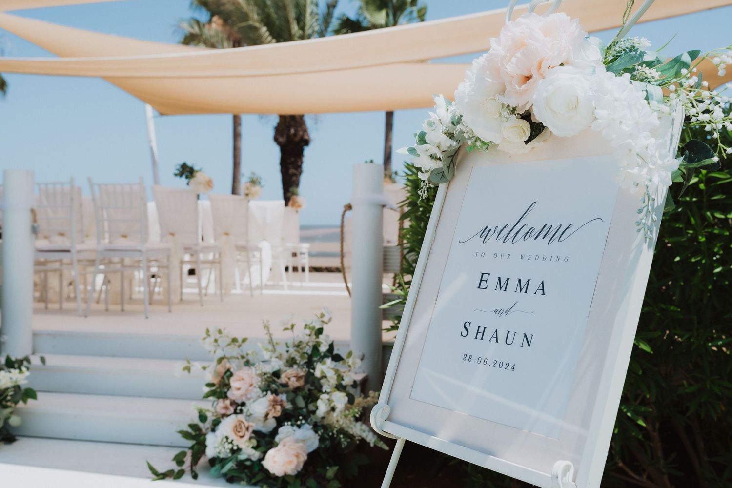 Waterfront wedding venue with white decor, draped canopy, and welcome sign.