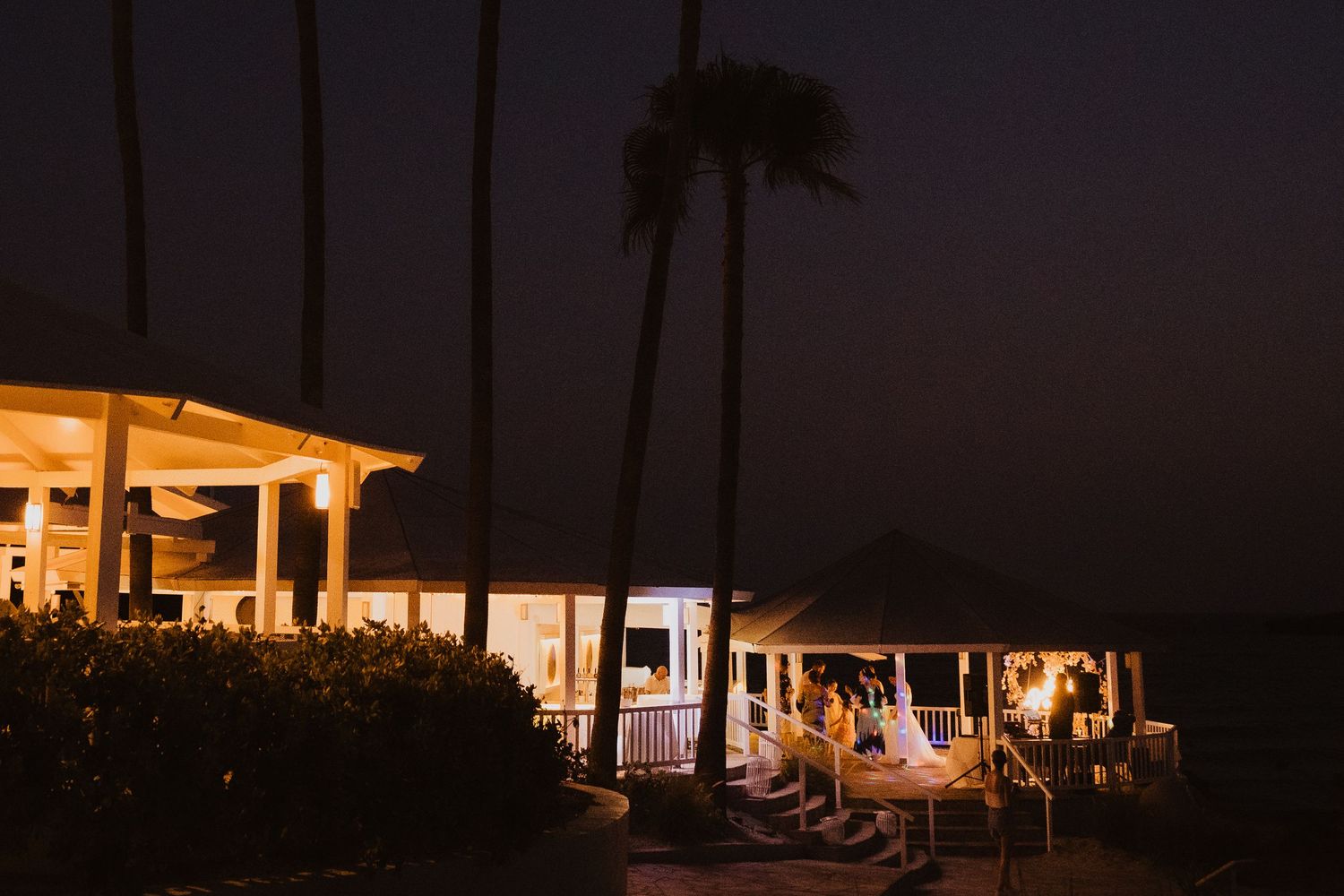 Illuminated beach pavilions and palm trees create a romantic nighttime coastal scene.