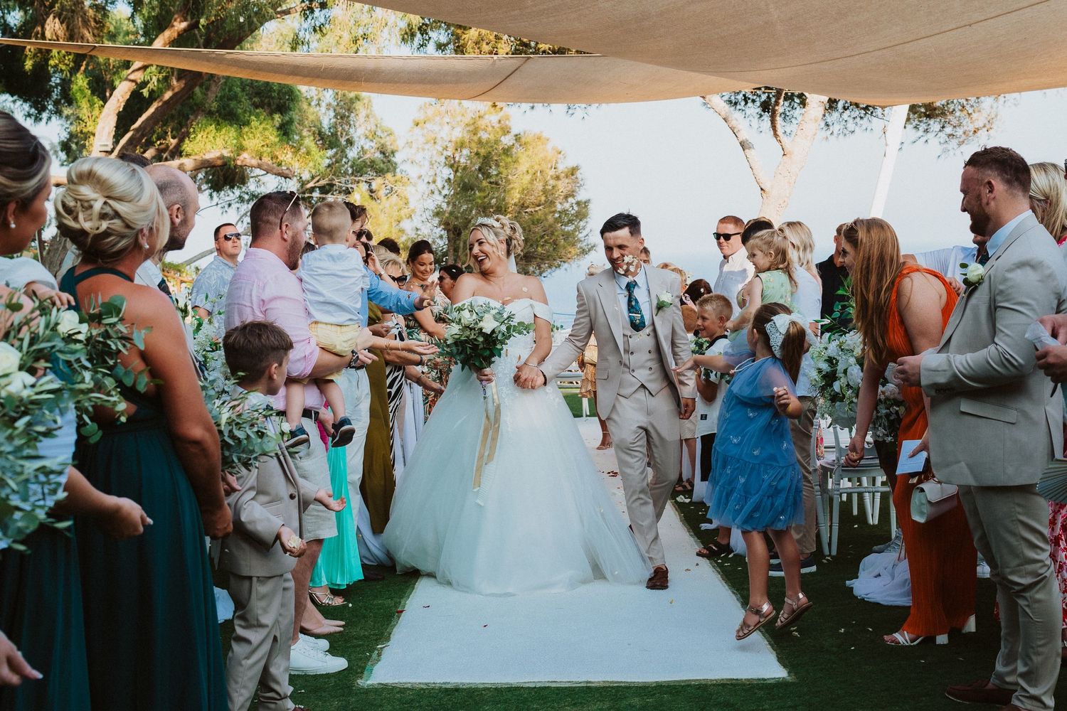 Wedding guests showering the aisle with confetti as a couple walks through during an outdoor ceremony.