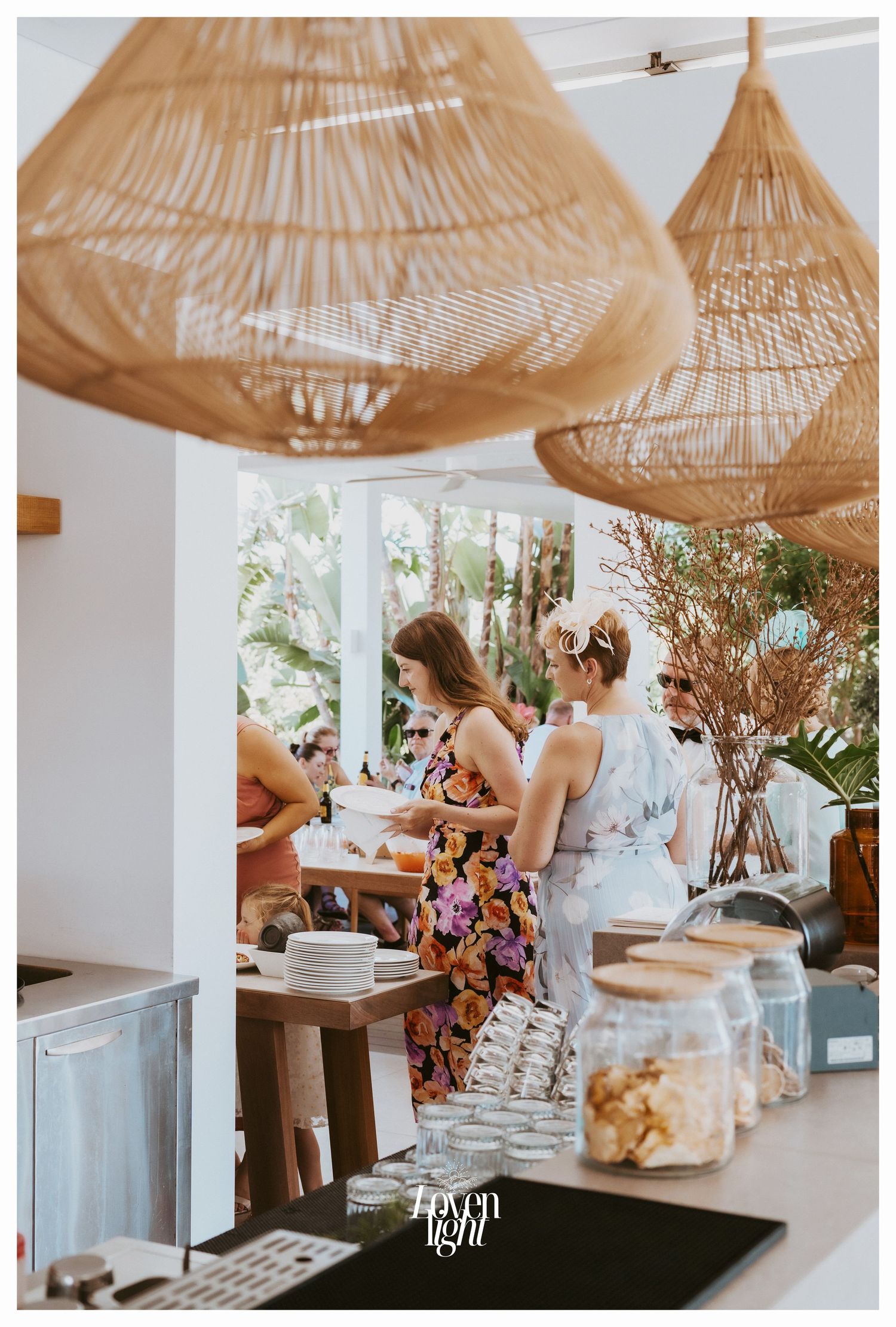 Guests serving food at a buffet table under boho-style woven pendant lights.