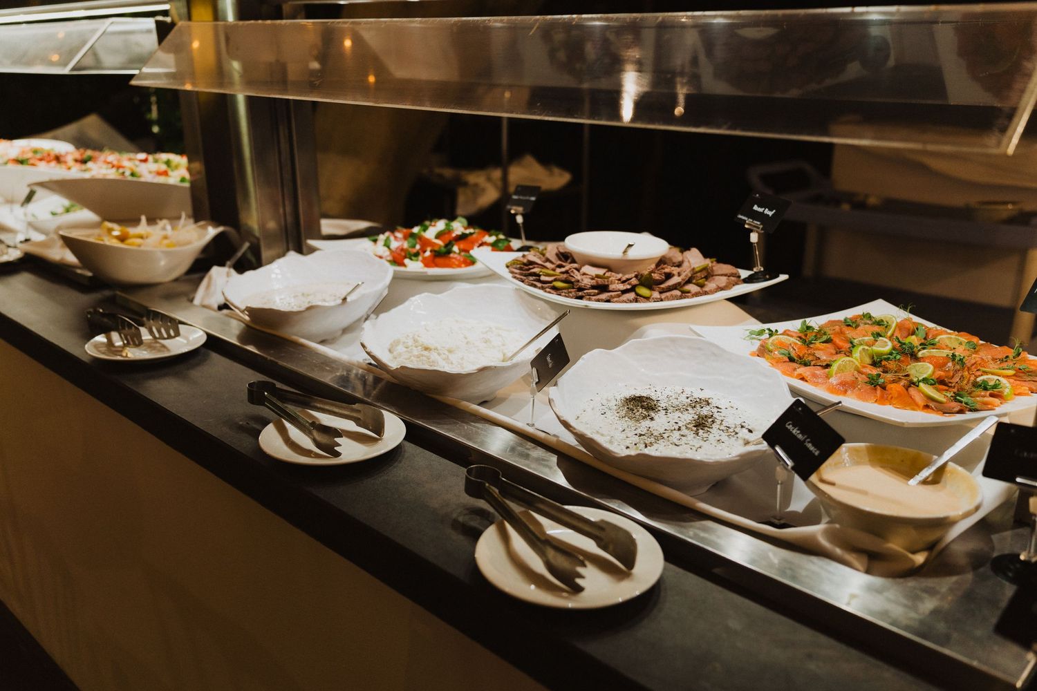 Catering buffet line with white serving dishes displaying various appetizers and entrees.