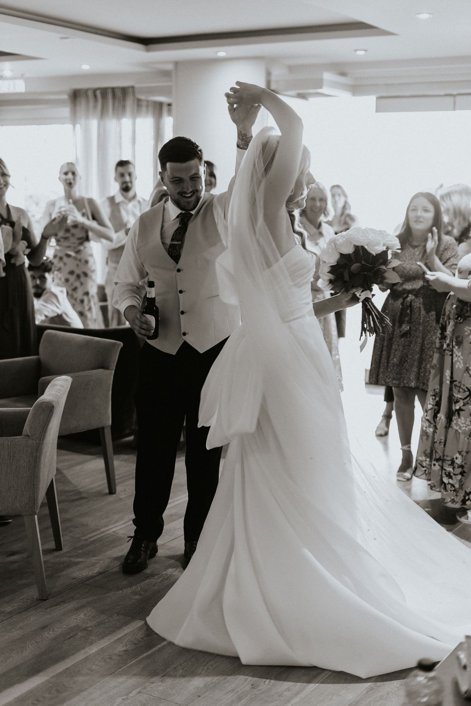 A couple shares their first dance at a wedding reception while guests look on from the background.