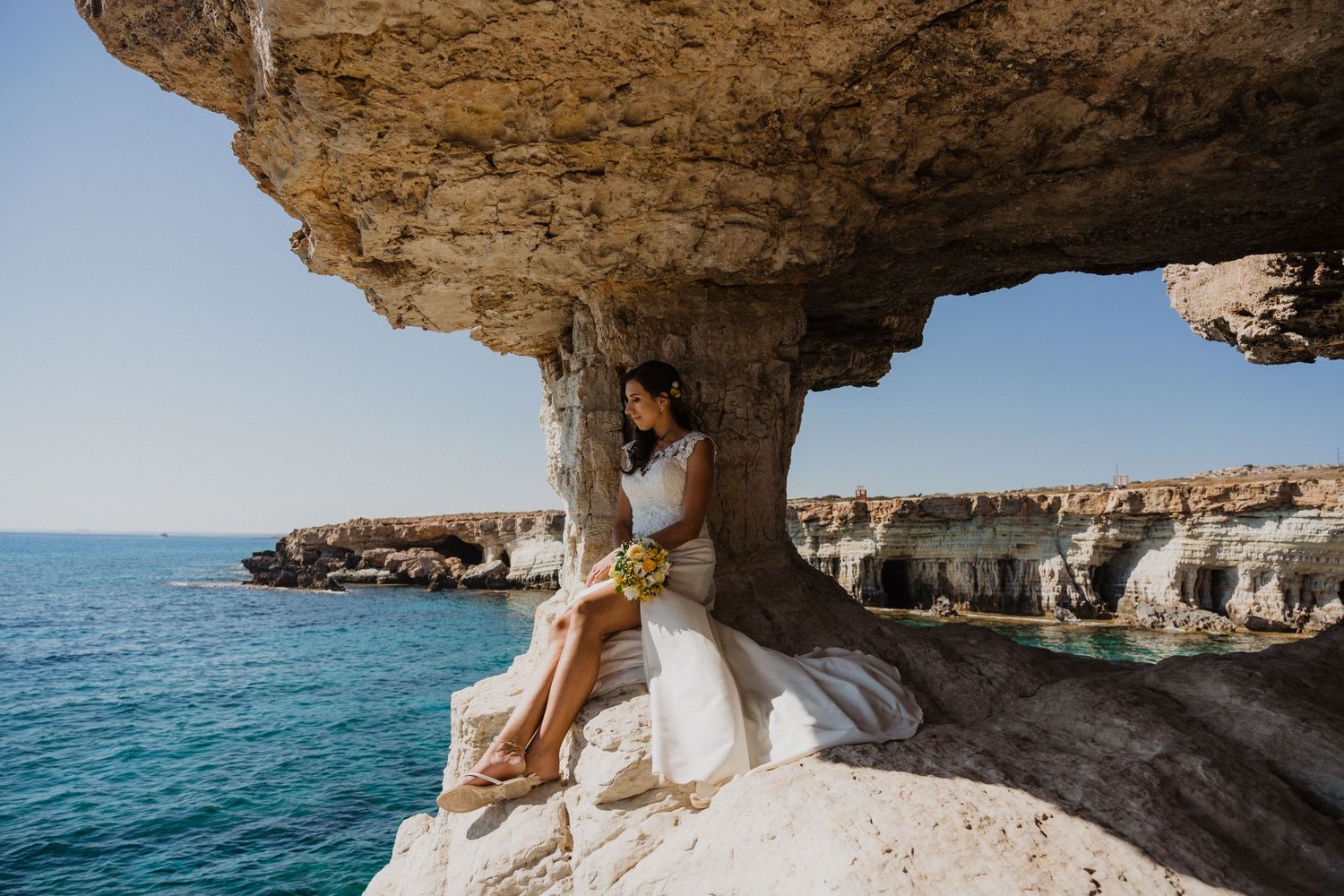 A stunning seaside wedding photo in a coastal cave overlooking blue Mediterranean waters.