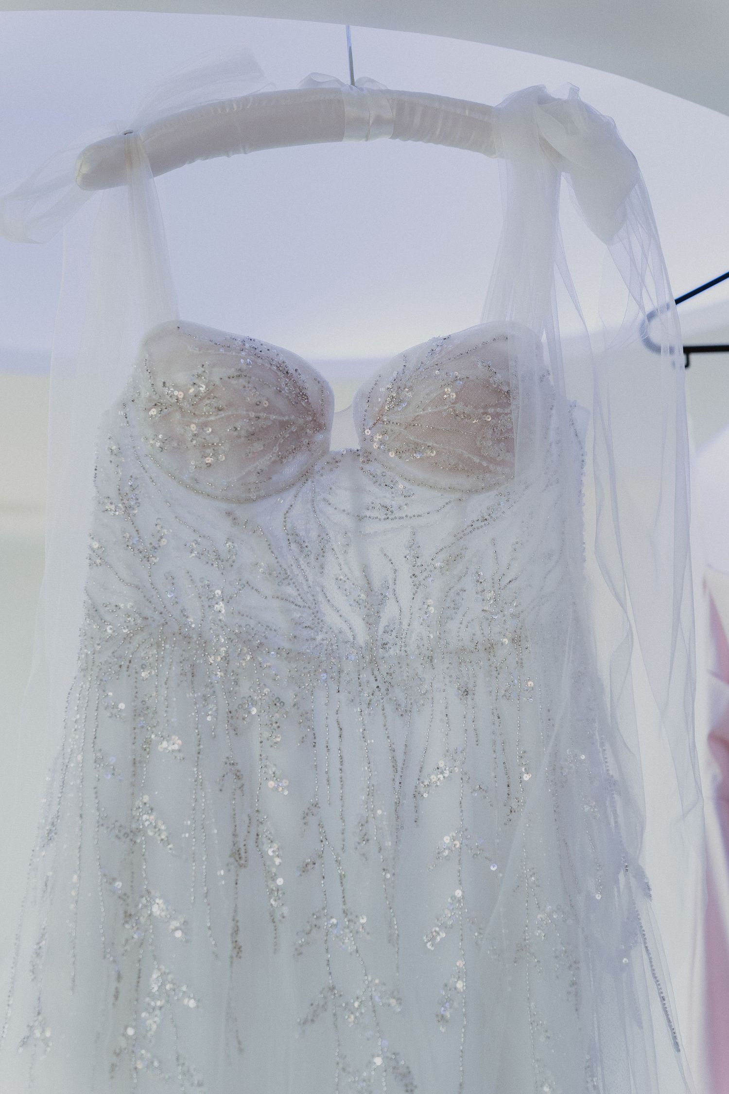 A delicate white wedding dress with sparkly details hanging on display.