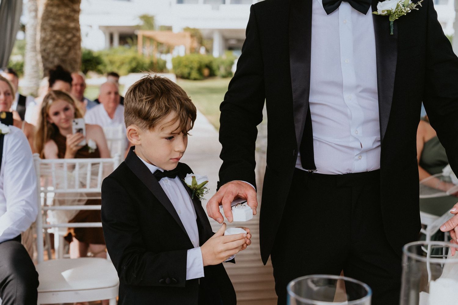 Ring bearer in formal attire carefully examining wedding rings during ceremony.