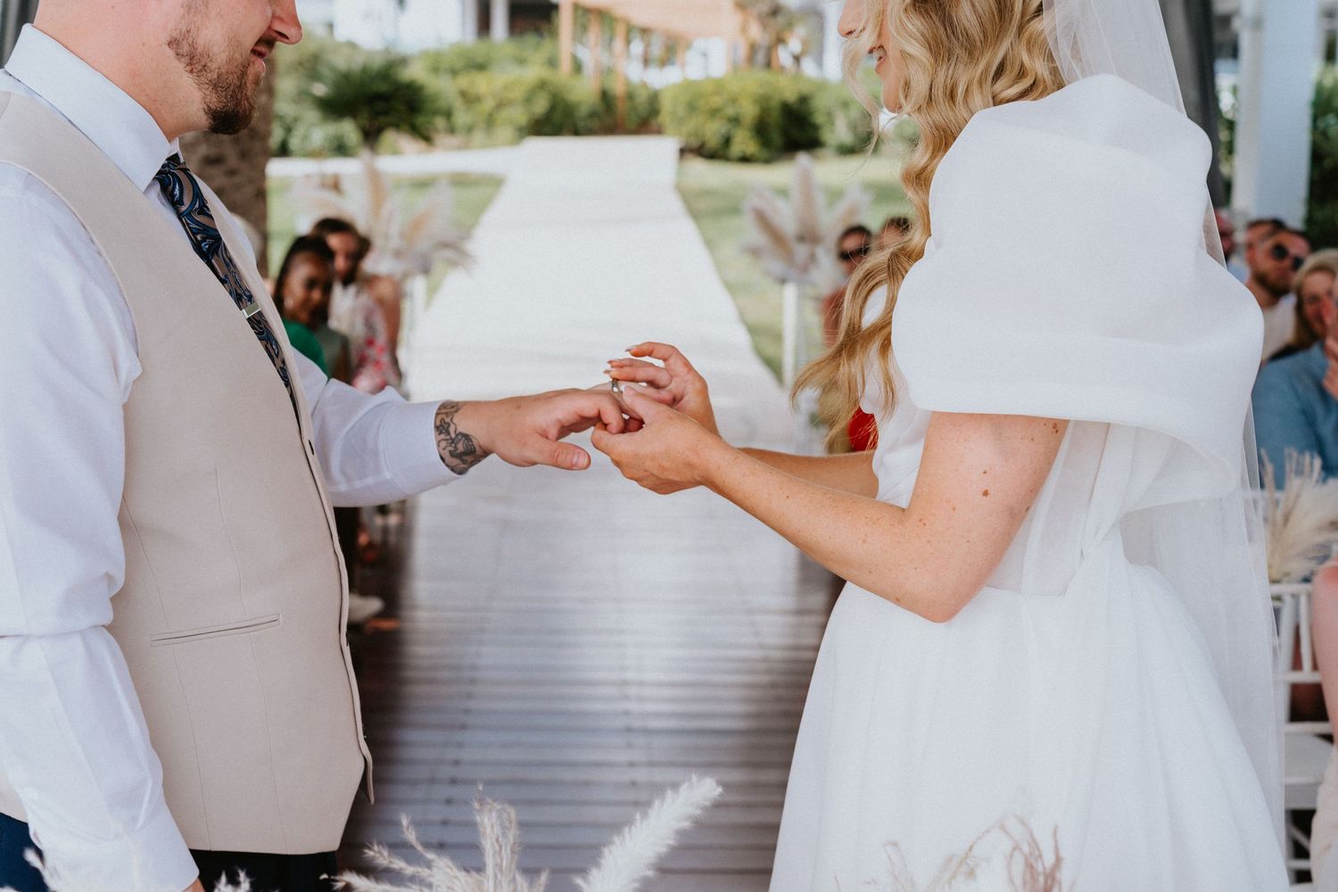 Intimate moment of ring exchange during outdoor waterfront wedding ceremony.