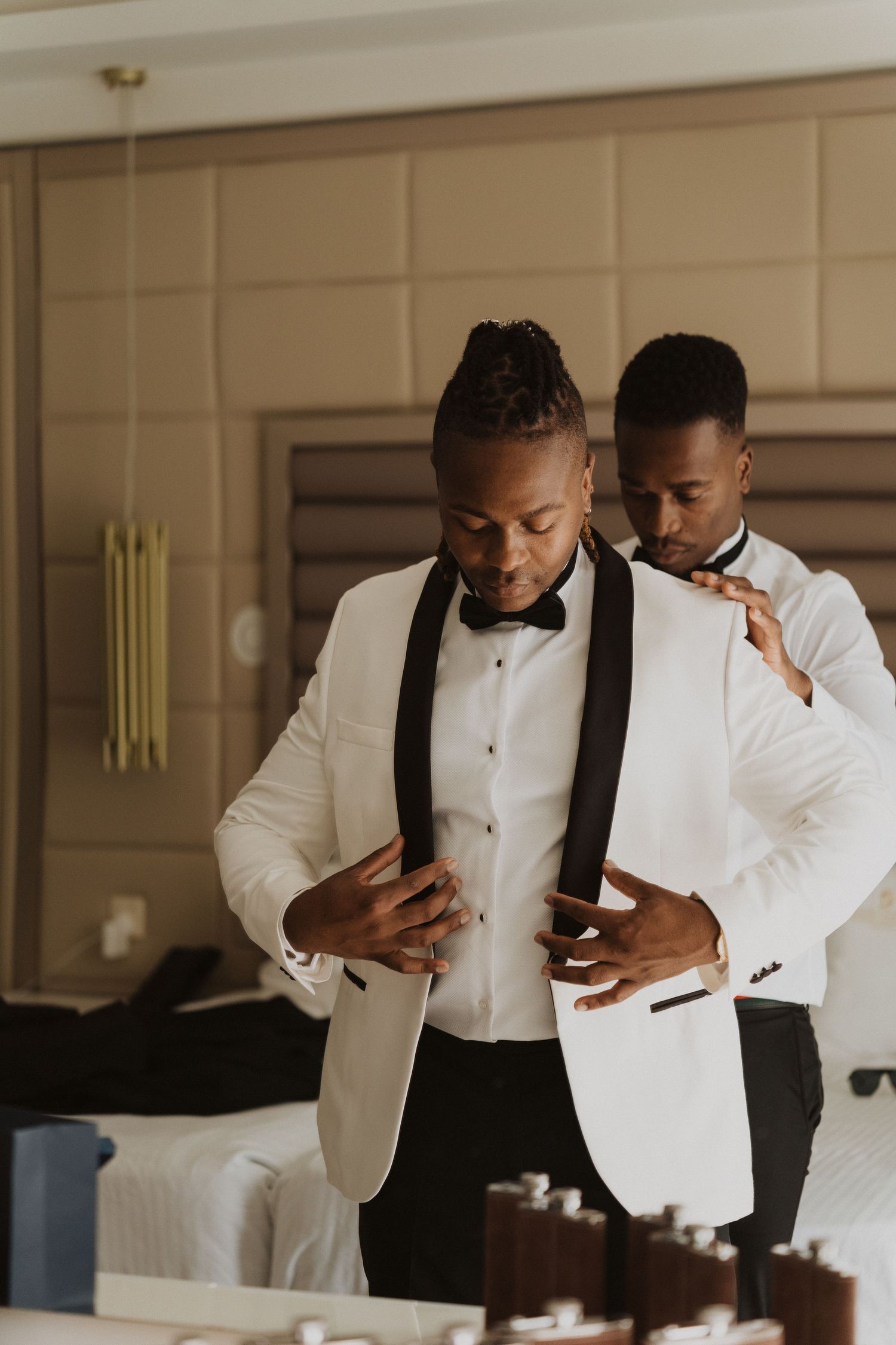 A person adjusts their white tuxedo jacket with black lapels while getting dressed.