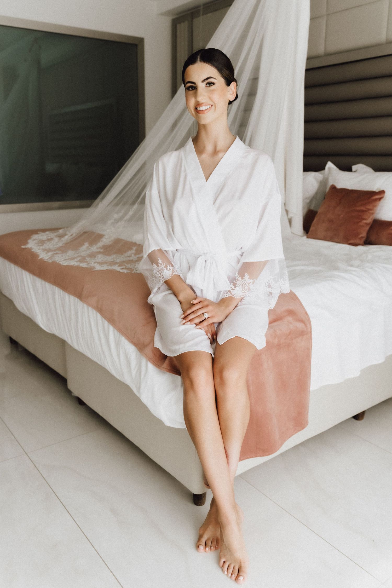 Pre-wedding moment in a bright modern bedroom with wedding dress in background.