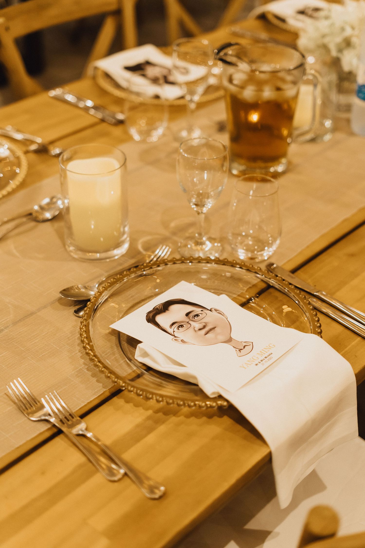Place setting with glassware, cutlery, and decorative plate on wooden table with drinks.