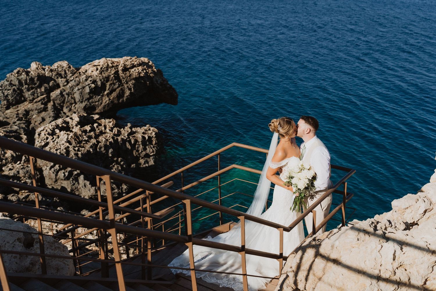 Couple shares intimate moment at scenic coastal wedding venue overlooking deep blue Mediterranean waters.