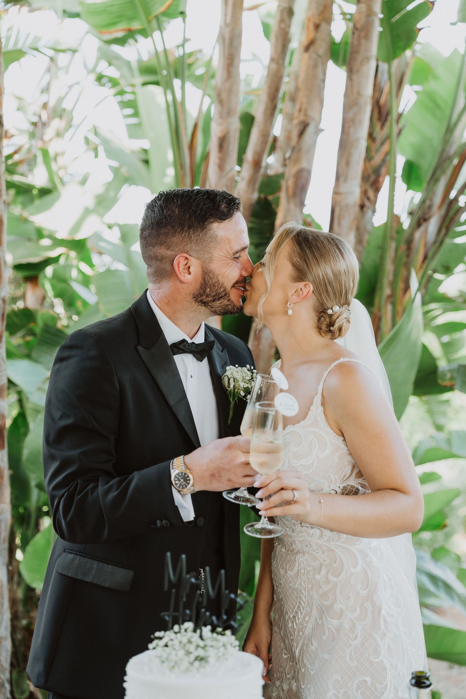Wedding couple shares a toast in a lush tropical garden setting with greenery in the background.
