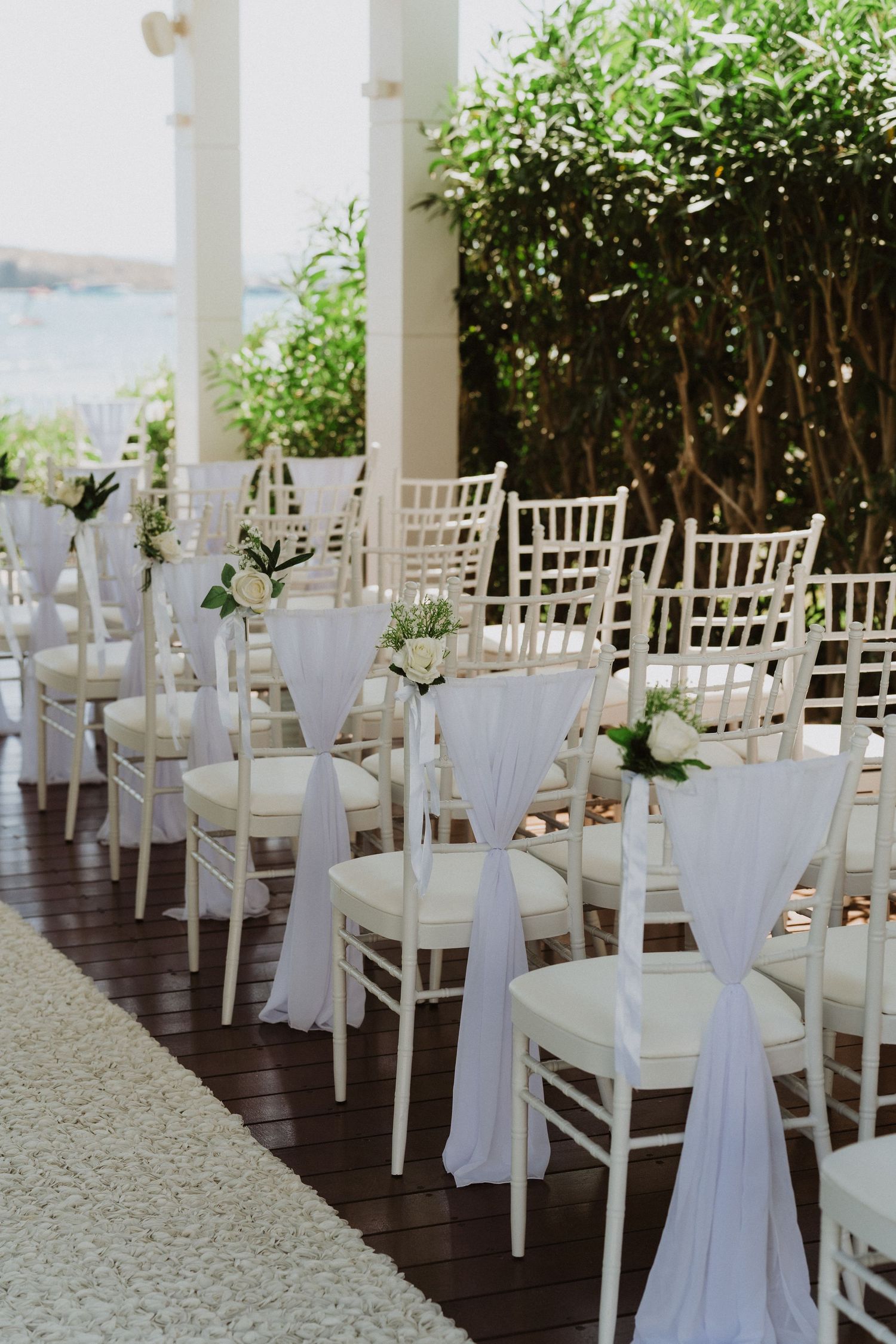 White chiavari chairs decorated with flowing white fabric sashes line up for an elegant outdoor wedding ceremony.